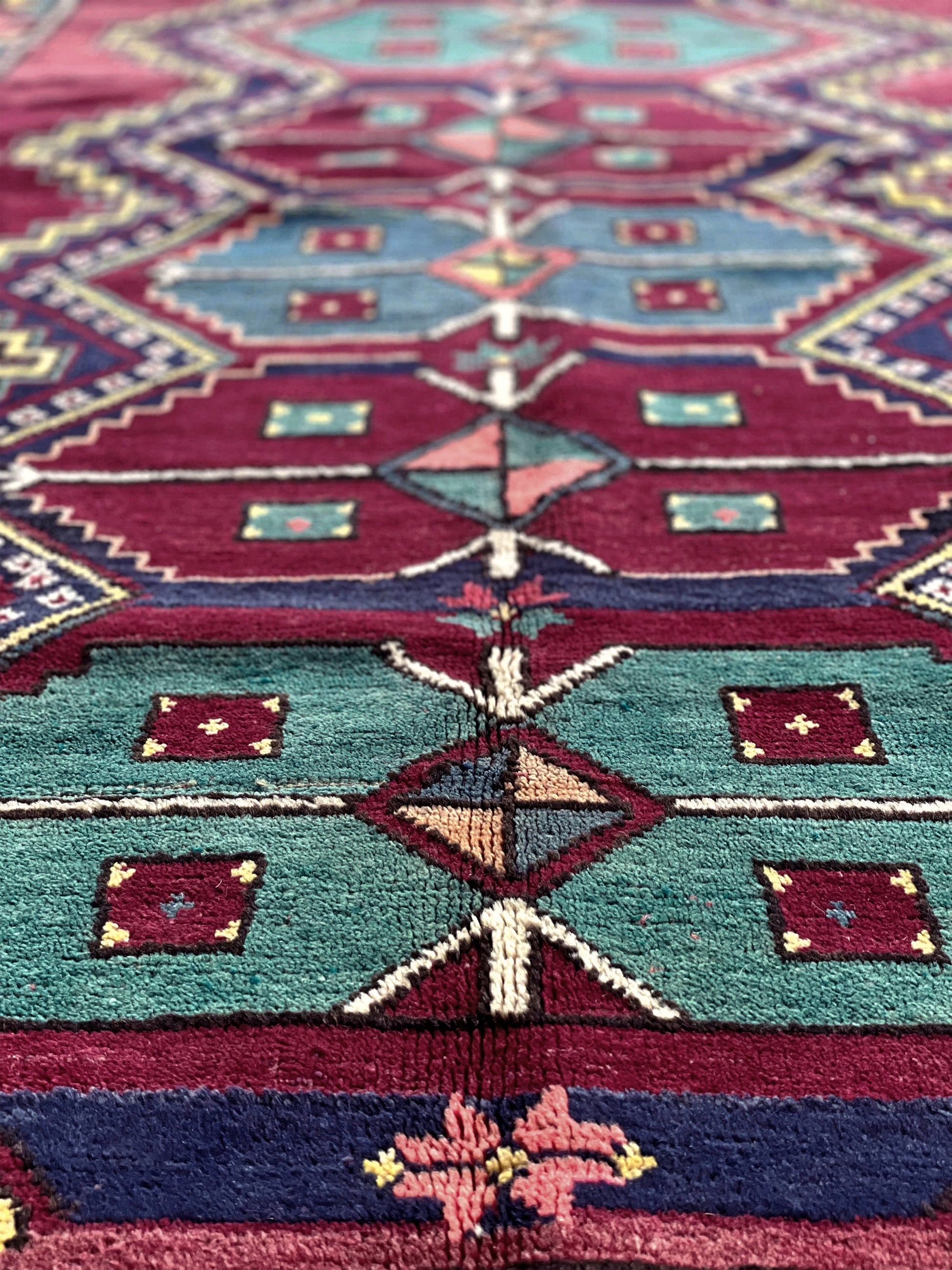 Close-up of a colorful patterned fabric with geometric designs. vintage kazak caucasian rug 6x9 burgundy field tribal geometric handmade wool 1940s antique style rug san francisco bay area rug shop indigo rugs