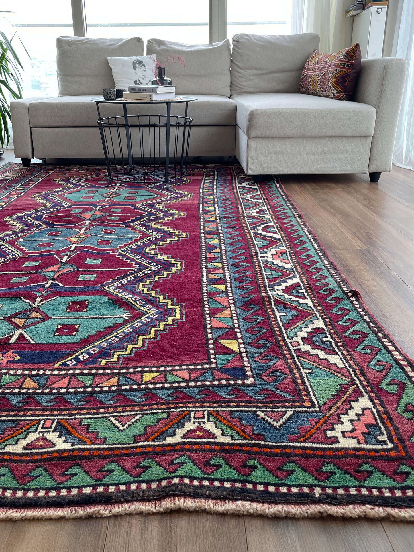 Living room with a colorful patterned rug, beige sectional sofa, and small table. vintage kazak caucasian rug 6x9 burgundy field tribal geometric handmade wool 1940s antique style rug san francisco bay area rug shop indigo rugs