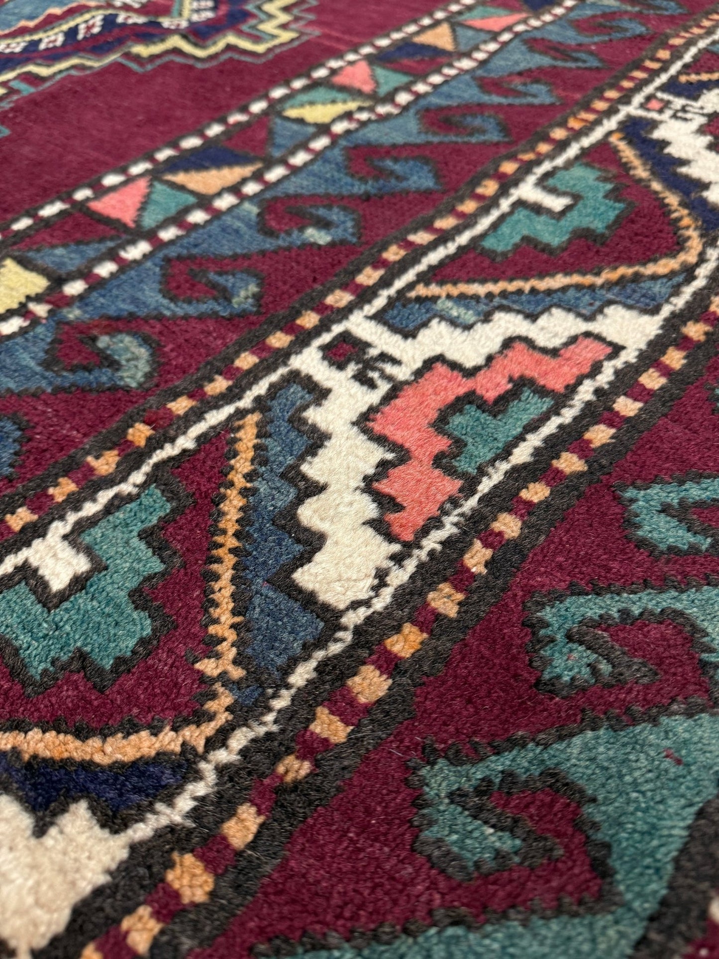 Close-up of a colorful patterned rug with geometric designs. vintage kazak caucasian rug 6x9 burgundy field tribal geometric handmade wool 1940s antique style rug san francisco bay area rug shop indigo rugs