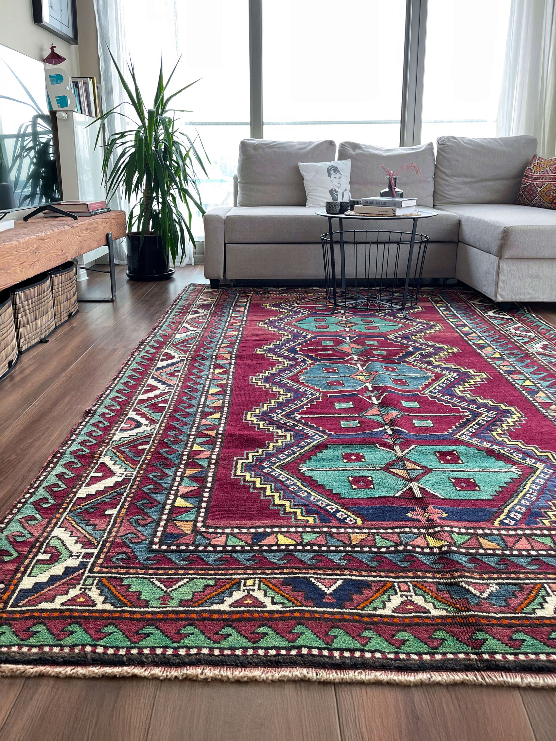 Colorful patterned rug in a living room with a sofa and decor. vintage kazak caucasian rug 6x9 burgundy field tribal geometric handmade wool 1940s antique style rug san francisco bay area rug shop indigo rugs