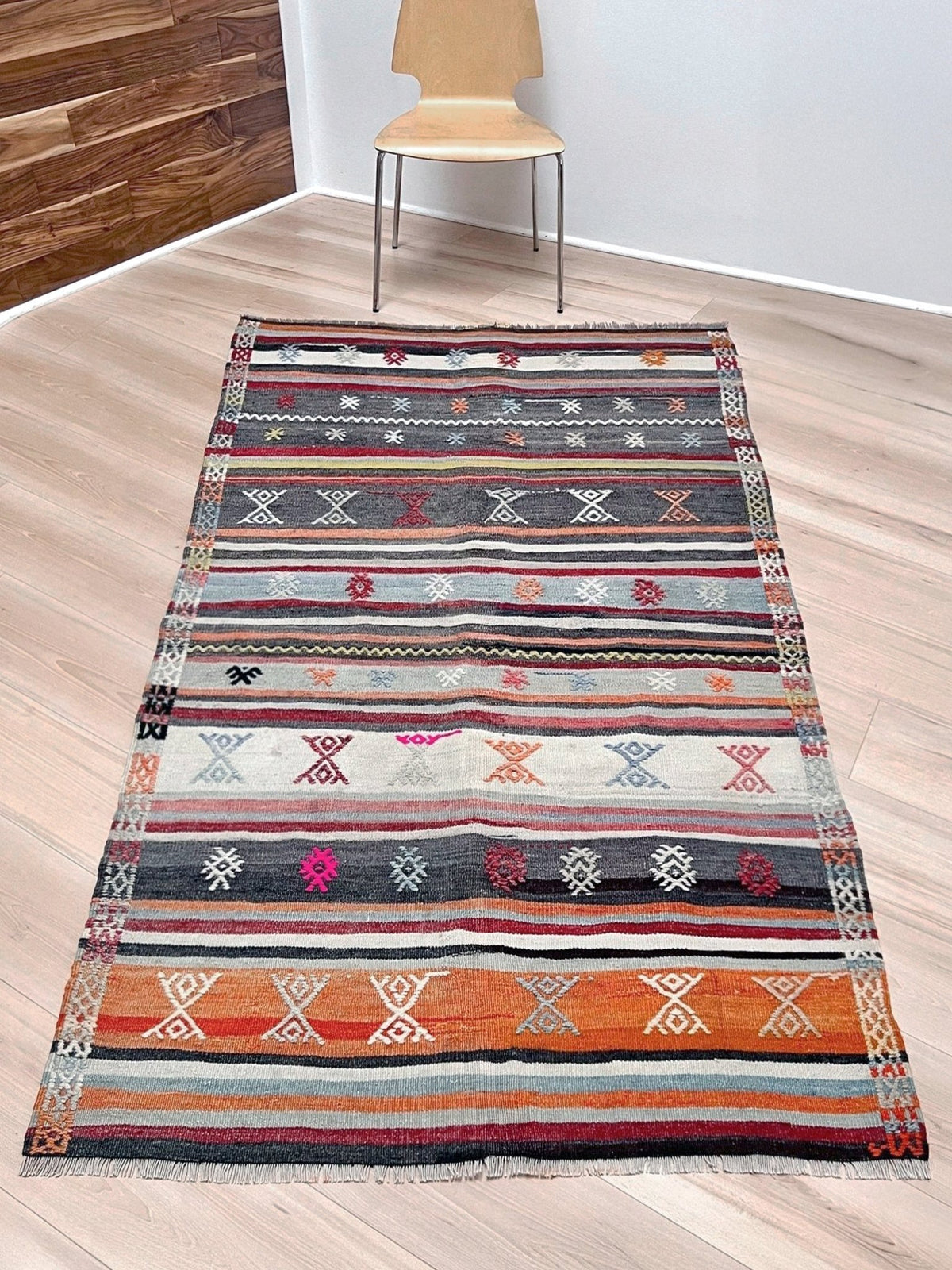 Multicolored striped rug with geometric patterns on a white background. Vintage Turkish striped kilim rug, 4x6, with tribal motifs in charcoal, ivory, sky blue, coral, and red bands.