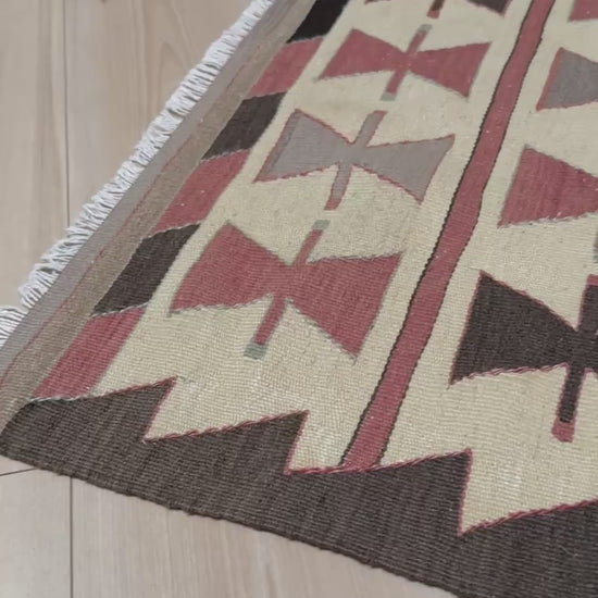 Vintage Mut Turkish kilim (3′1″ × 4′10″) with bow-tie tribal motifs and a stepped medallion in warm ivory, muted rose, taupe-grey, chocolate brown. Handmade Turkish flatweave, 1970s, sold by Indigo Rugs in Burlingame / San Francisco Bay Area.