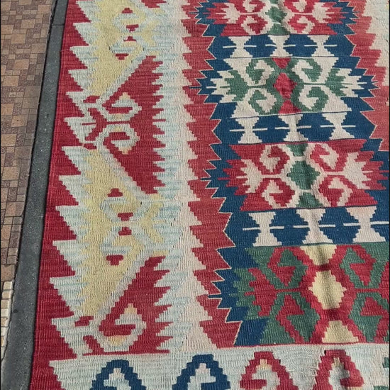 Woven turkish kilim rug with geometric pattern featuring red, blue, and beige colors. 