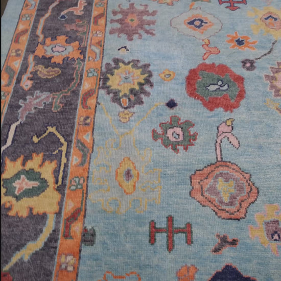 Pale turquoise Turkish Oushak rug with charcoal border, coral orange framing, and colorful abstract floral motifs, hand-knotted wool 8x10 area rug from Indigo Rugs Burlingame Bay Area.