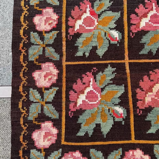 Vintage Moldovan Rose Kilim Rug from the 1950s, featuring a bold black ground with vibrant pink rose motifs and orange lines woven throughout. Handwoven with care, this flatweave rug adds unique character and style to living rooms, bedrooms, nurseries, kitchens, or dining areas. Free shipping included.