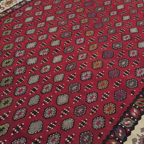 Decorative rug with intricate pattern on a red background. Vintage Pirot kilim with warm madder red field and repeating geometric medallions, handwoven wool flatweave rug with ivory border, approx. 7x10.
