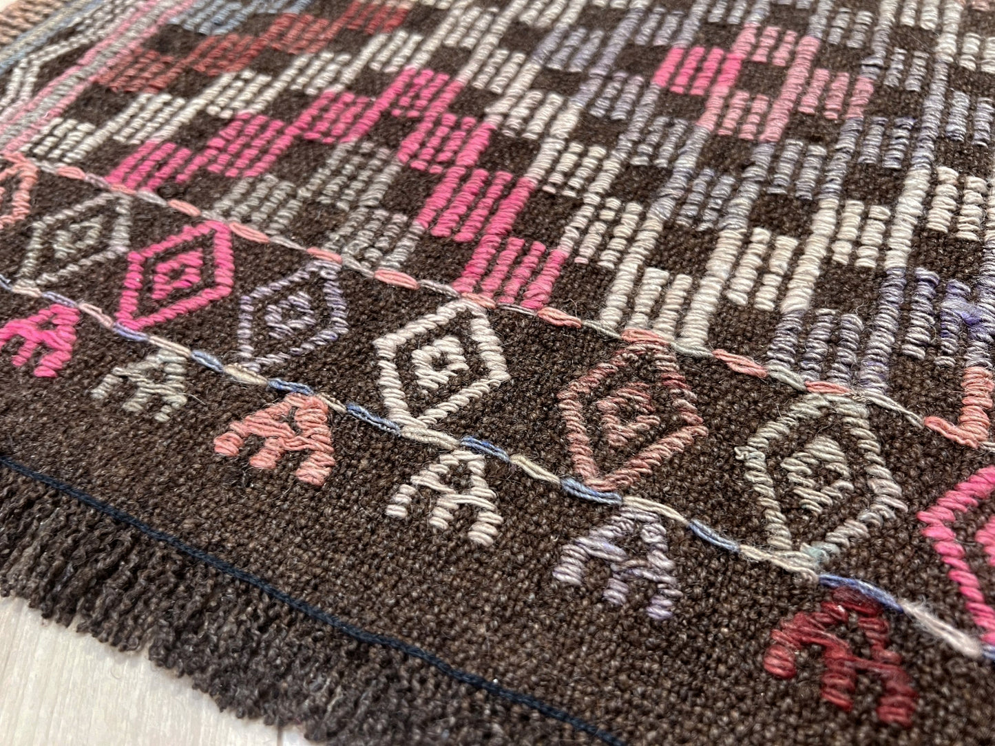 Close-up of a textured fabric with geometric patterns in brown, pink, and white. Earthy Vintage Turkish cicim kilim rug, 5x7 Anatolian flatweave with embroidered geometric motifs in brown, ivory, dusty rose, and slate blue