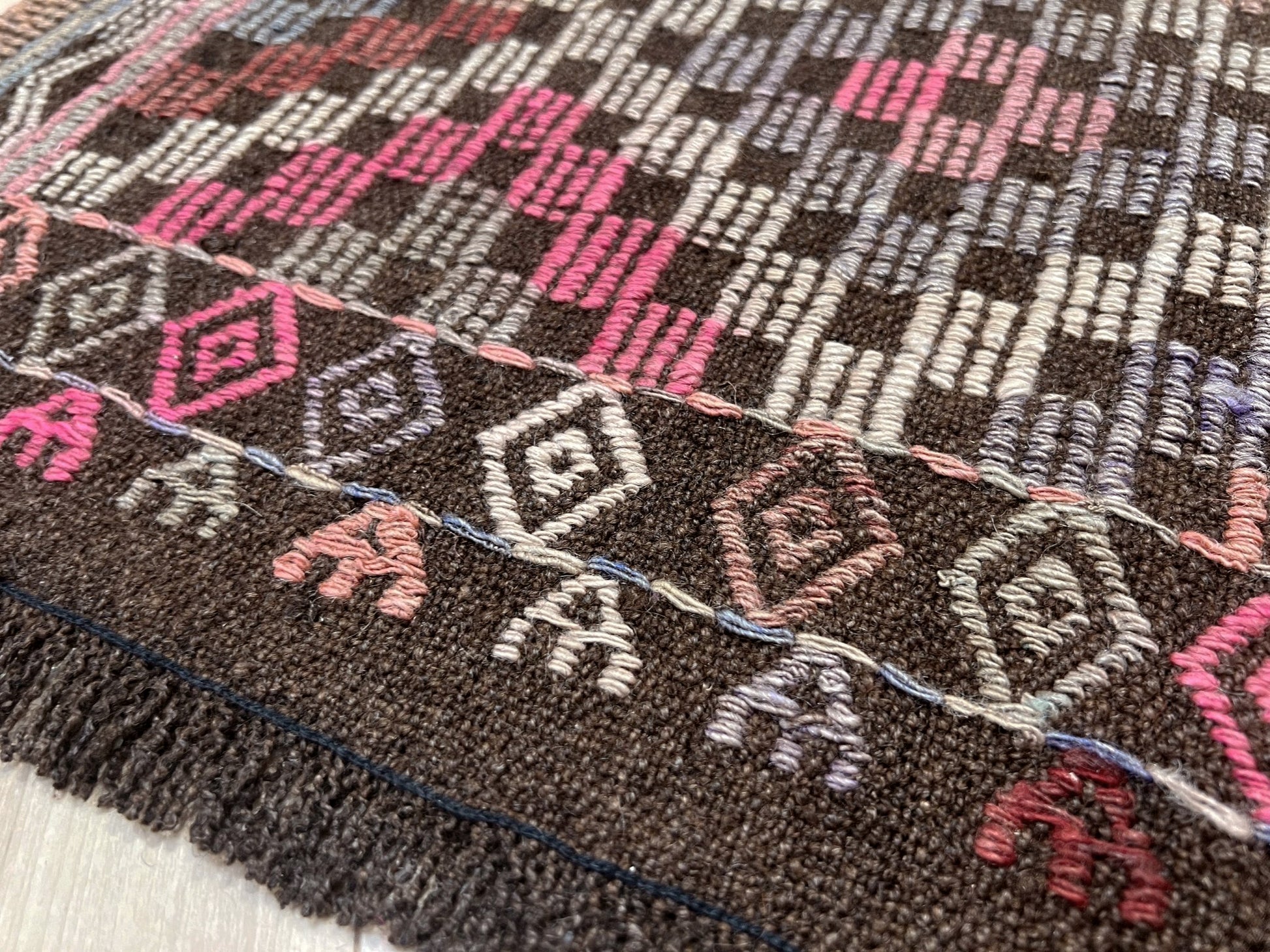 Close-up of a textured fabric with geometric patterns in brown, pink, and white. Earthy Vintage Turkish cicim kilim rug, 5x7 Anatolian flatweave with embroidered geometric motifs in brown, ivory, dusty rose, and slate blue