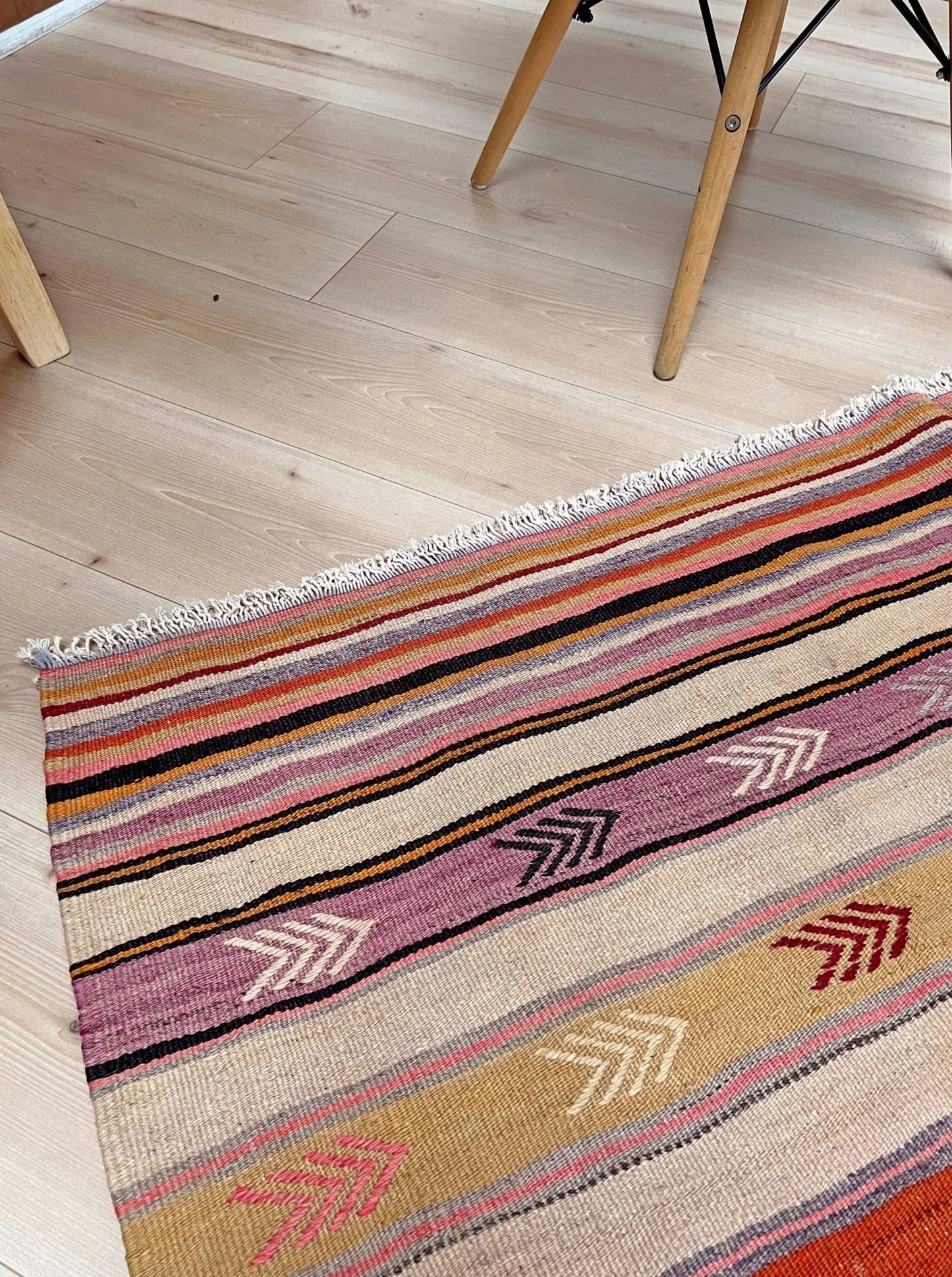 Multicolored striped rug with arrow patterns on a wooden floor. Vintage Anatolian kilim rug, 6x8 with horizontal arrow motifs in sun-washed tones.