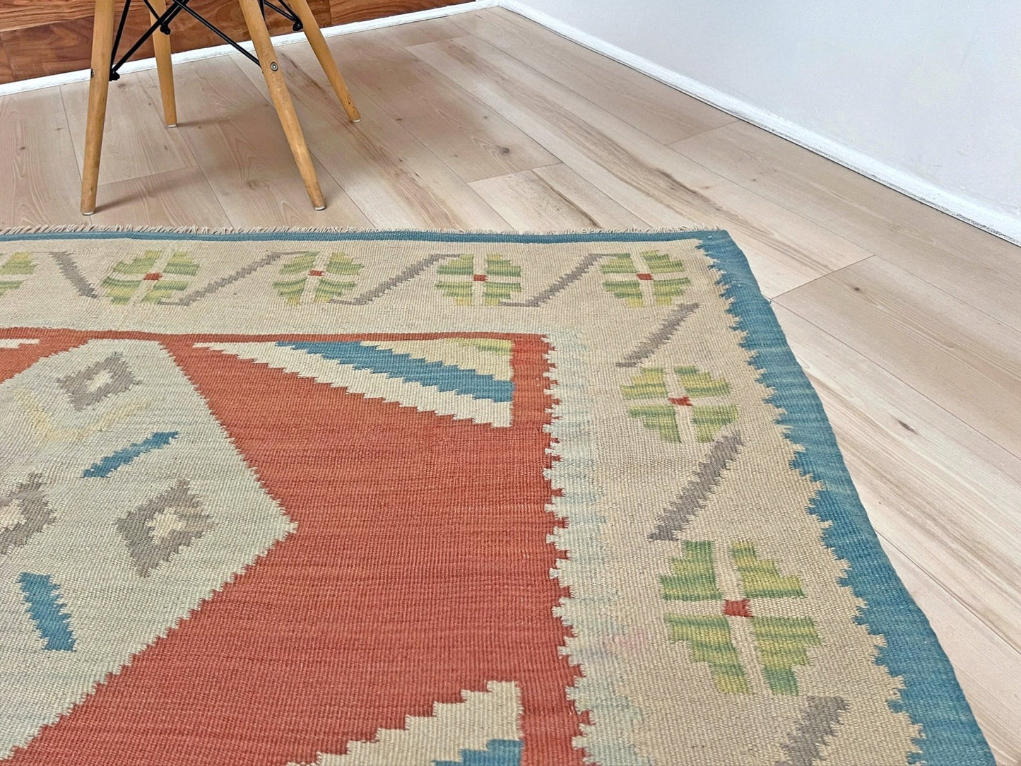 Colorful geometric-patterned rug on a wooden floor. Vintage Turkish Malatya kilim rug with coral red field and diamond medallions, handwoven Anatolian flatweave 5x8 geometric wool rug