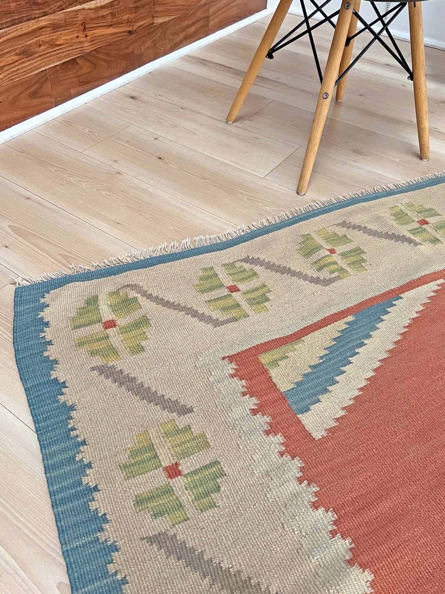 Patterned rug on a wooden floor with a chair visible. Vintage Turkish Malatya kilim rug with coral red field and diamond medallions, handwoven Anatolian flatweave 5x8 geometric wool rug