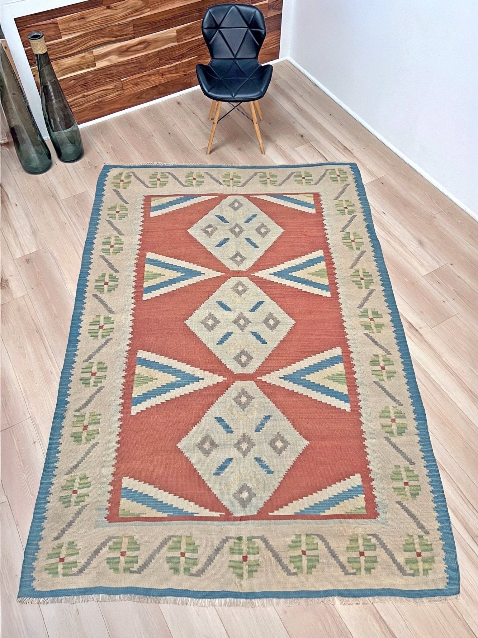 Decorative rug with geometric pattern on a wooden floor. Vintage Turkish Malatya kilim rug with coral red field and diamond medallions, handwoven Anatolian flatweave 5x8 geometric wool rug