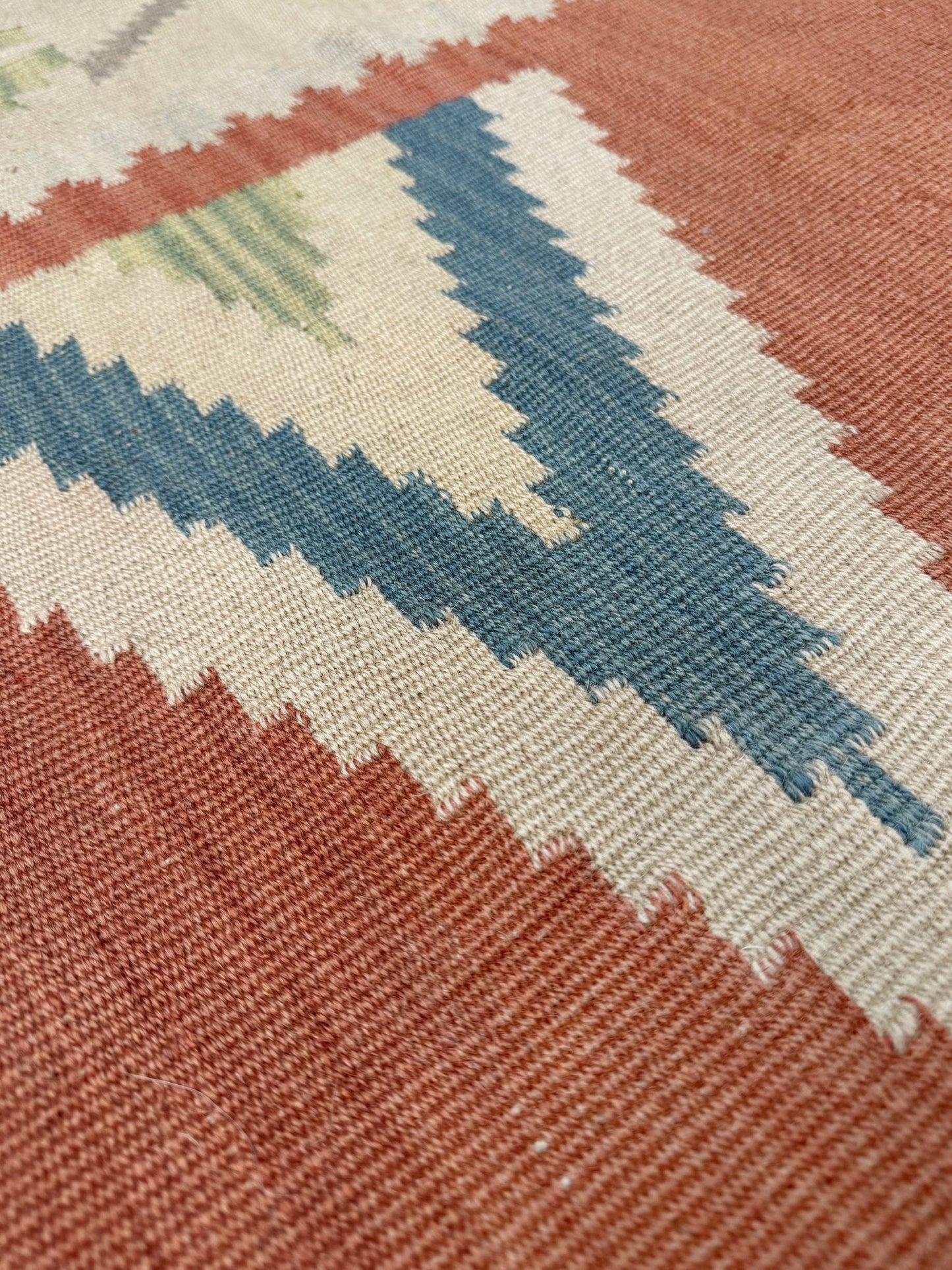 Close-up of a patterned rug with blue, white, and red colors. Vintage Turkish Malatya kilim rug with coral red field and diamond medallions, handwoven Anatolian flatweave 5x8 geometric wool rug