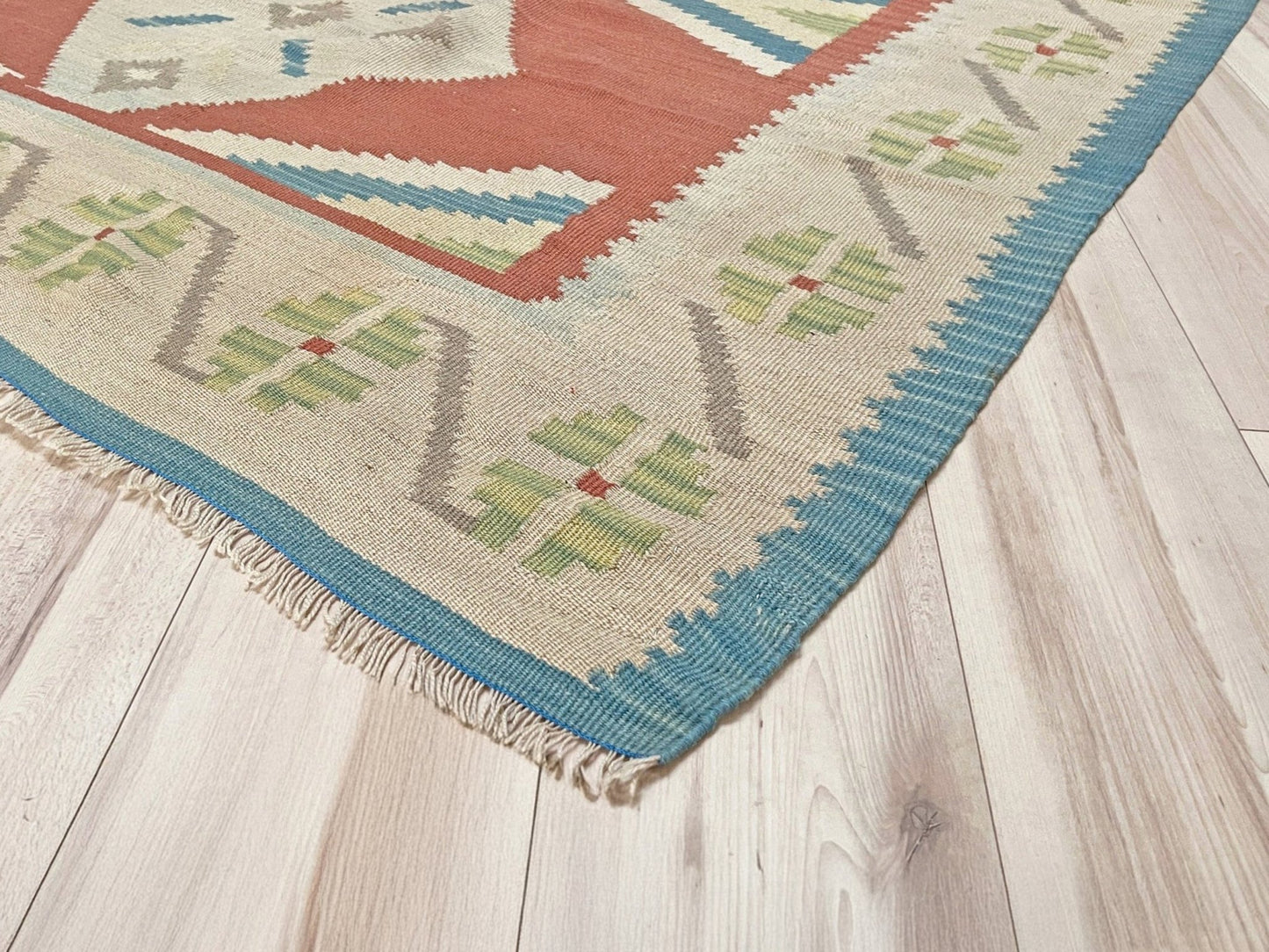 Colorful woven rug with geometric pattern on a wooden floor. Vintage Turkish Malatya kilim rug with coral red field and diamond medallions, handwoven Anatolian flatweave 5x8 geometric wool rug
