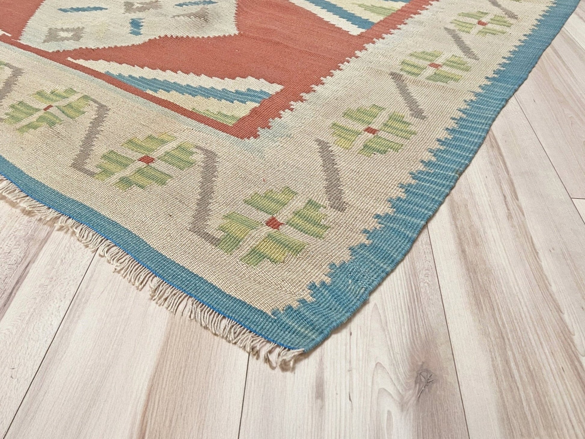 Colorful woven rug with geometric pattern on a wooden floor. Vintage Turkish Malatya kilim rug with coral red field and diamond medallions, handwoven Anatolian flatweave 5x8 geometric wool rug