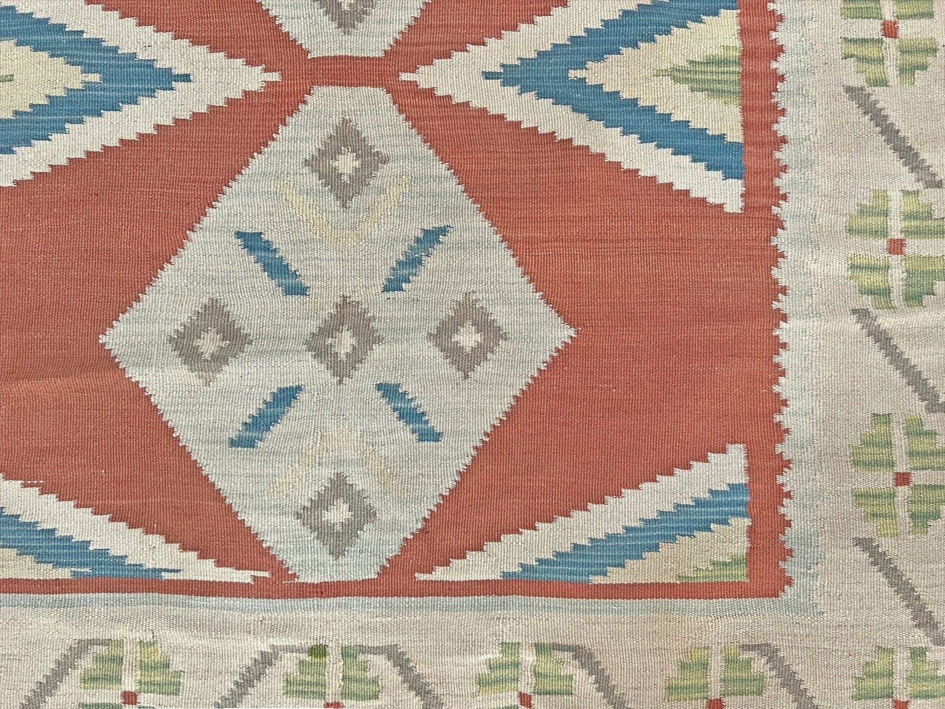 Close-up of a geometric patterned rug with red, blue, and beige colors. Vintage Turkish Malatya kilim rug with coral red field and diamond medallions, handwoven Anatolian flatweave 5x8 geometric wool rug