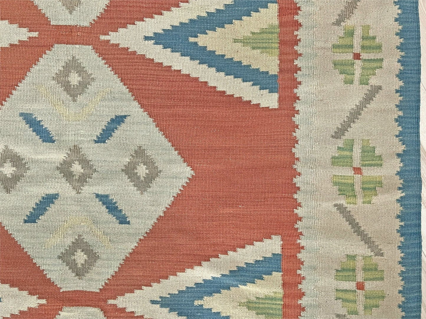 Close-up of a patterned fabric with geometric designs in red, blue, green, and beige. Vintage Turkish Malatya kilim rug with coral red field and diamond medallions, handwoven Anatolian flatweave 5x8 geometric wool rug