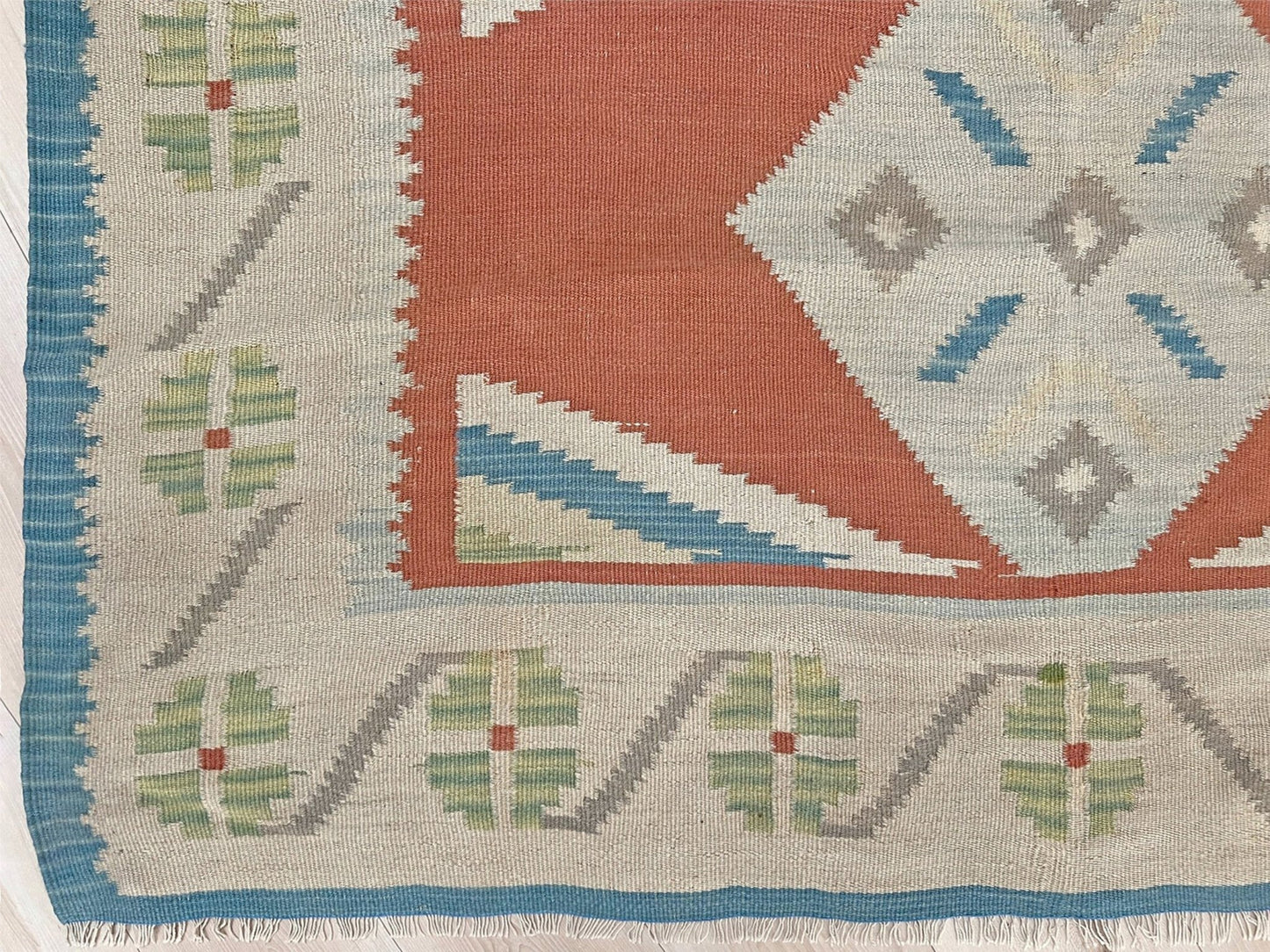 Close-up of a patterned rug with geometric designs in red, blue, green, and beige. Vintage Turkish Malatya kilim rug with coral red field and diamond medallions, handwoven Anatolian flatweave 5x8 geometric wool rug
