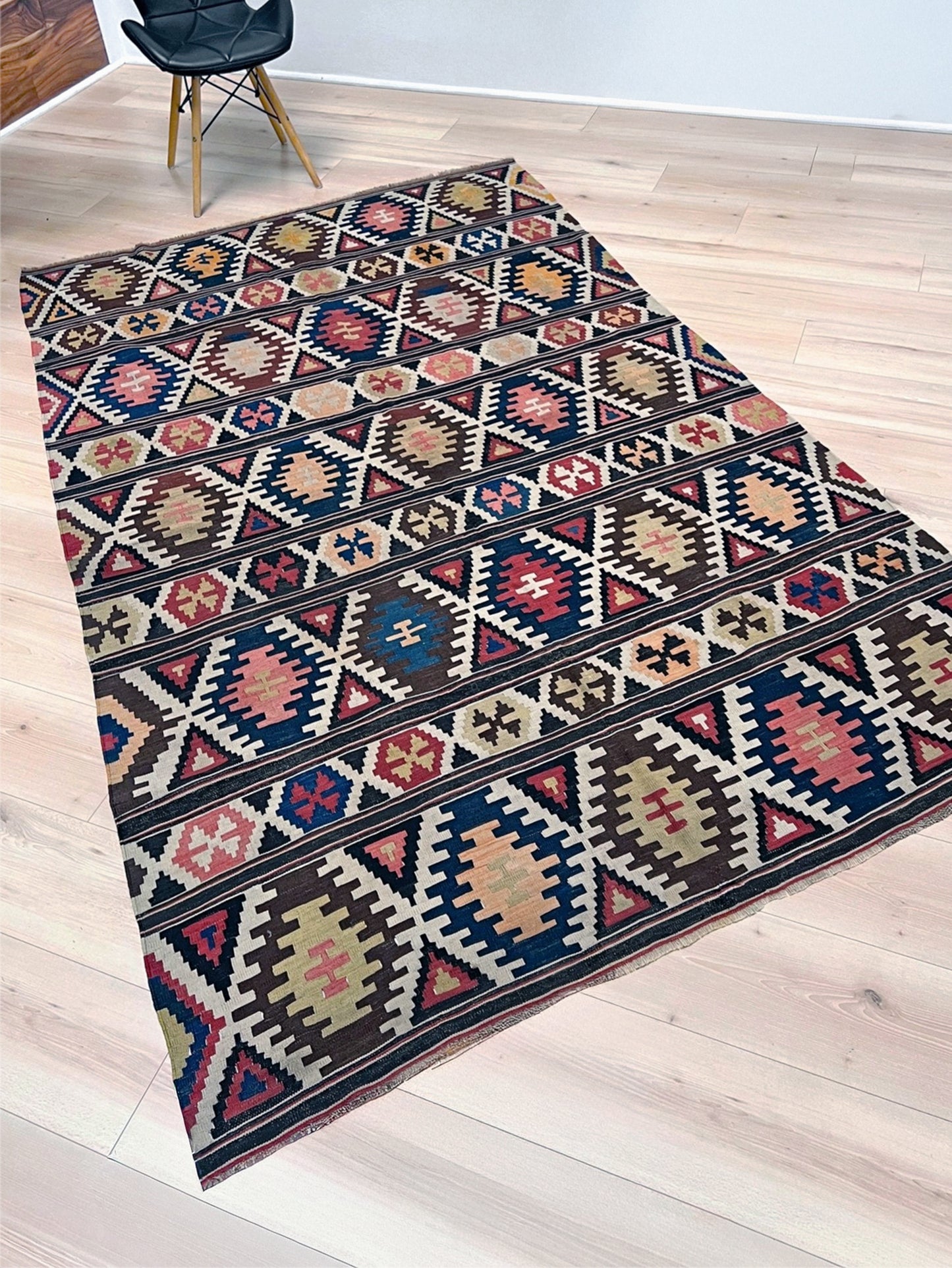 Multicolored patterned rug on a wooden floor. Vintage Caucasian Kazak tribal kilim rug with geometric medallions in beige, red, blue, and brown — handmade flatweave 5x8