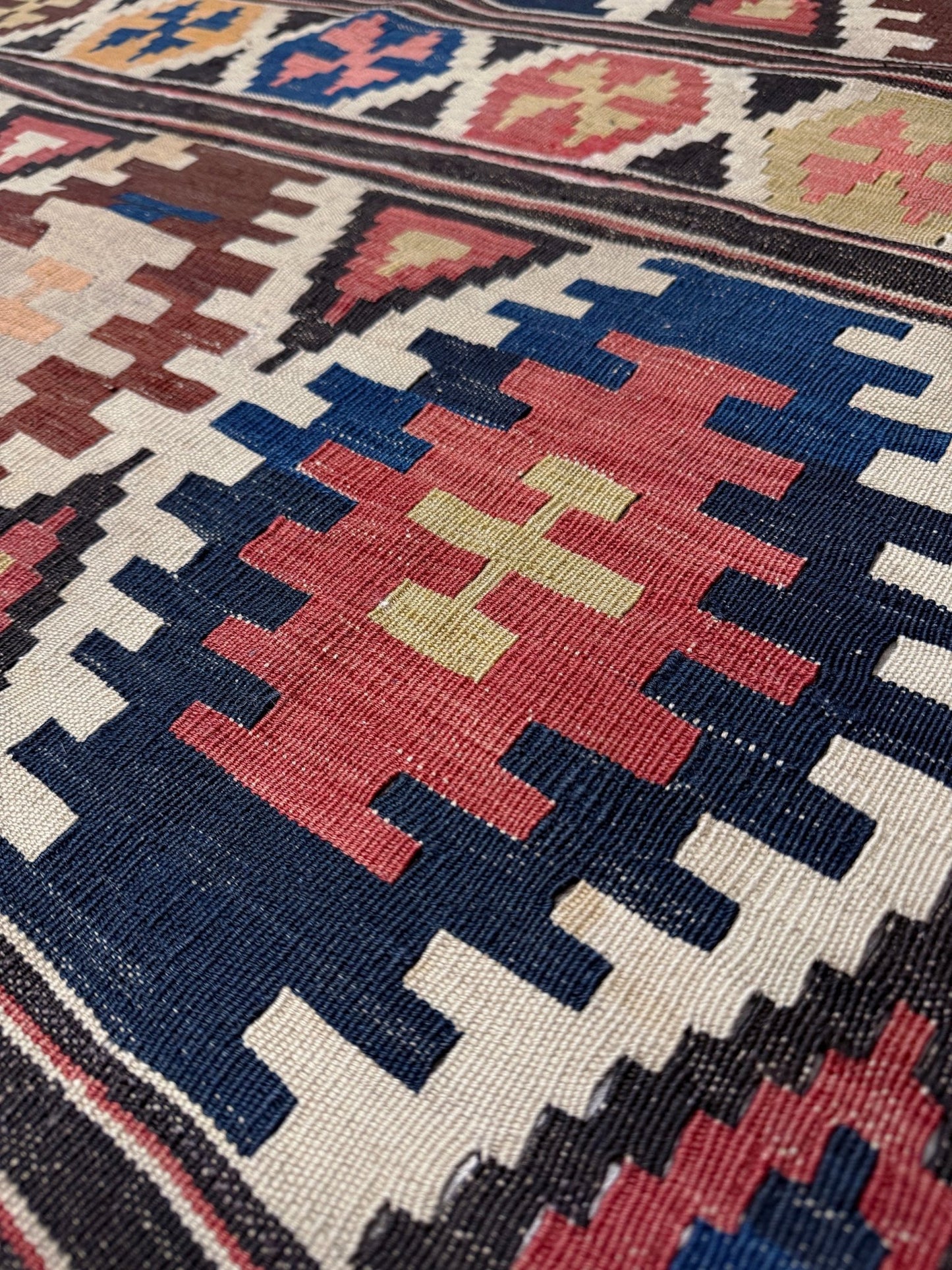 Close-up of a patterned rug with geometric design. Vintage Caucasian Kazak tribal kilim rug with geometric medallions in beige, red, blue, and brown — handmade flatweave 5x8