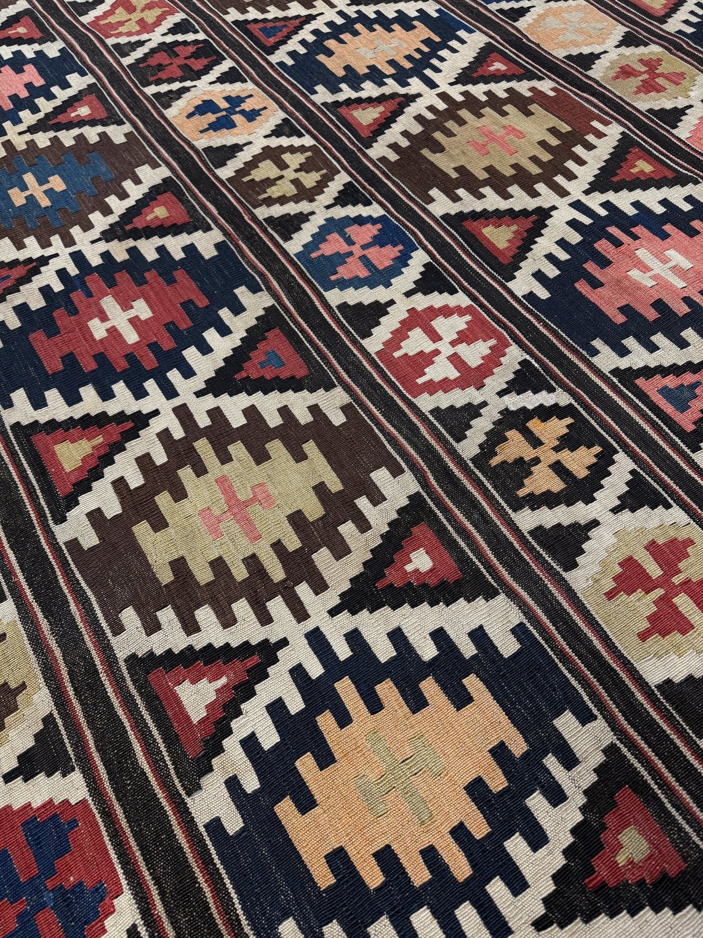 Close-up of a patterned rug with geometric designs in various colors. Vintage Caucasian Kazak tribal kilim rug with geometric medallions in beige, red, blue, and brown — handmade flatweave 5x8