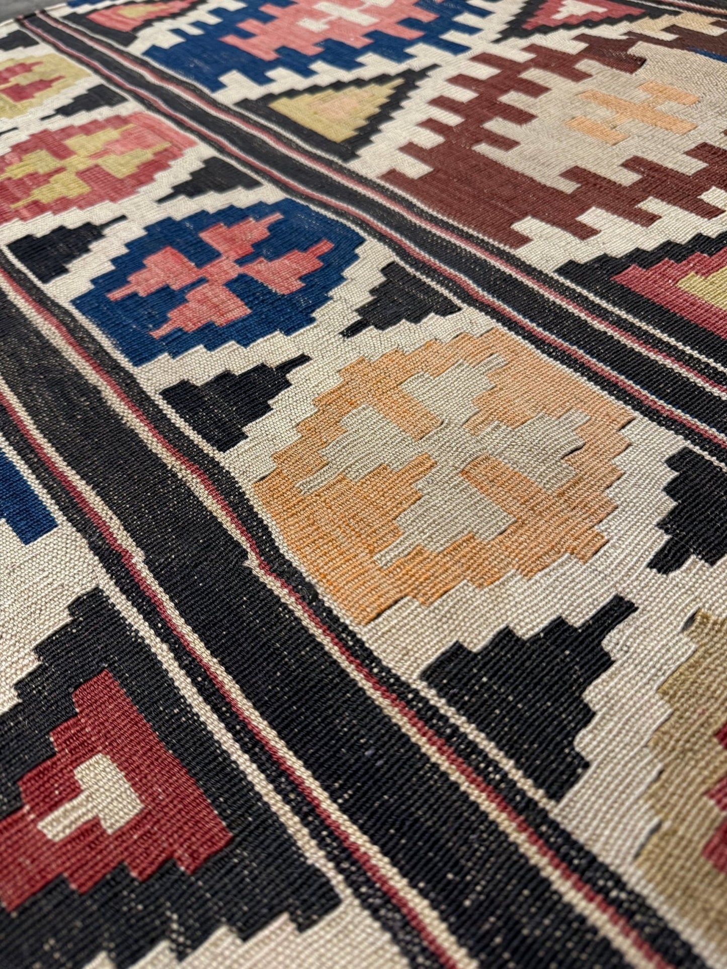 Close-up of a patterned rug with geometric design. Vintage Caucasian Kazak tribal kilim rug with geometric medallions in beige, red, blue, and brown — handmade flatweave 5x8