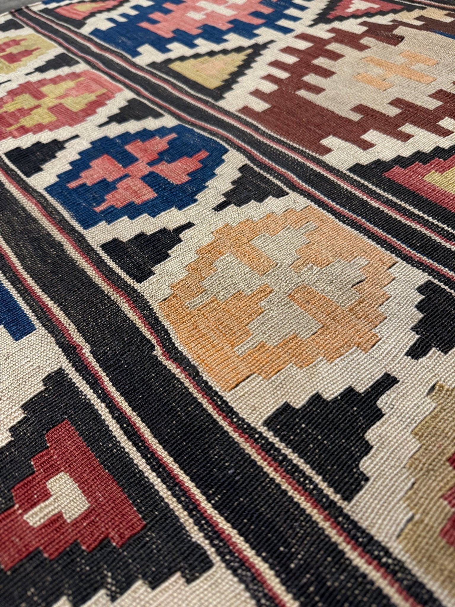 Close-up of a patterned rug with geometric design. Vintage Caucasian Kazak tribal kilim rug with geometric medallions in beige, red, blue, and brown — handmade flatweave 5x8
