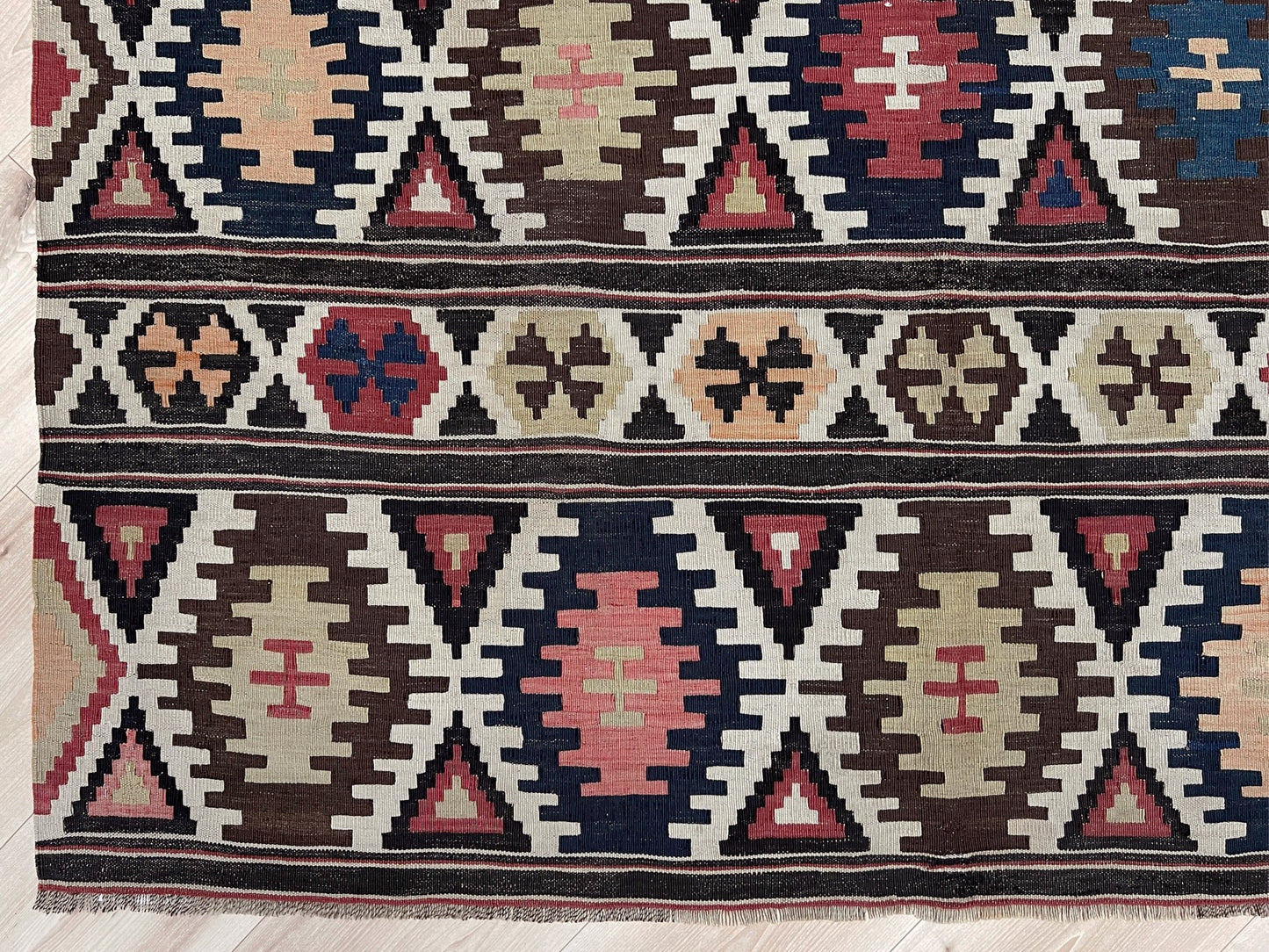Patterned rug with geometric design on a wooden floor. Vintage Caucasian Kazak tribal kilim rug with geometric medallions in beige, red, blue, and brown — handmade flatweave 5x8