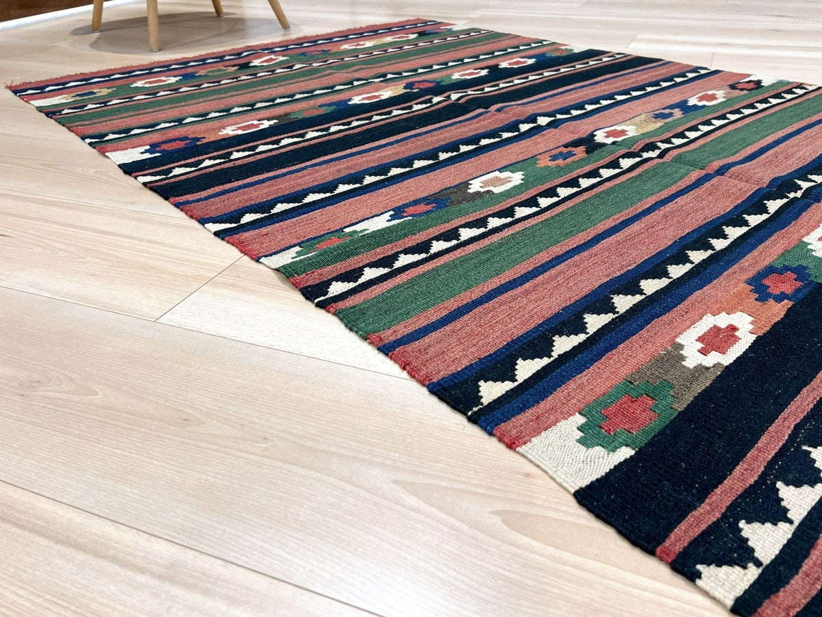 A rectangular kilim-style area rug with a multicolor geometric and floral pattern, laid out on a light-colored wooden floor.