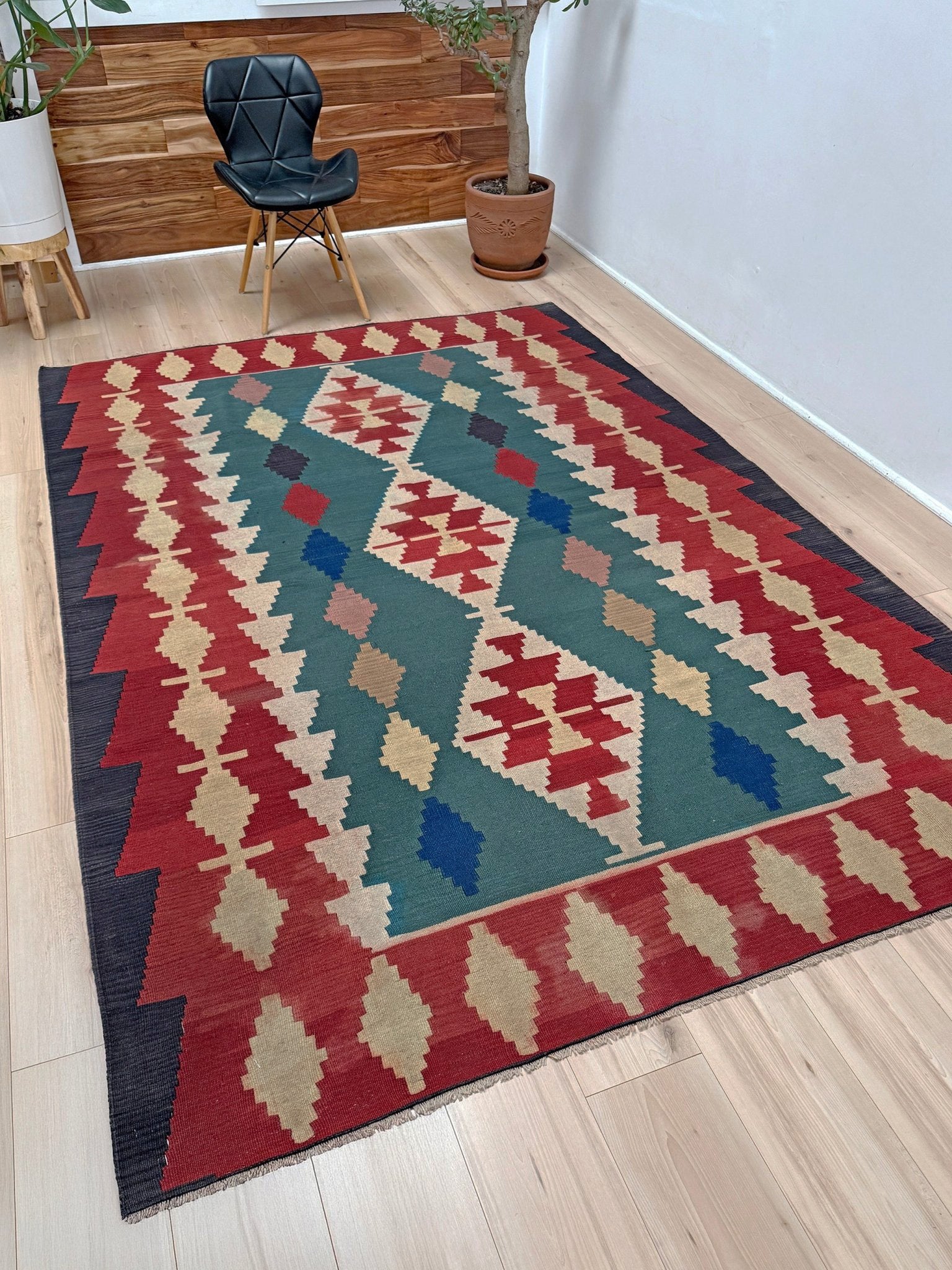 A rectangular woven area rug with a Southwestern geometric pattern in red, teal, beige, blue, and dark navy, displayed on a light wood floor in a modern room setting.