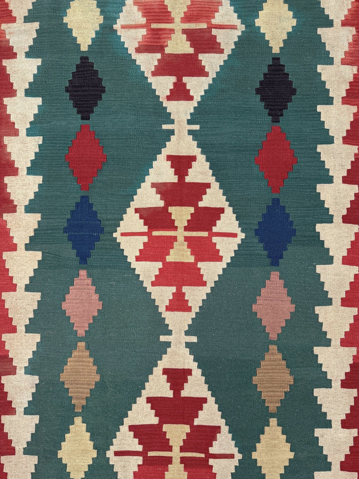 A close-up of a woven textile with a Southwestern geometric pattern featuring red, navy, pink, beige, and teal diamond and triangle motifs.