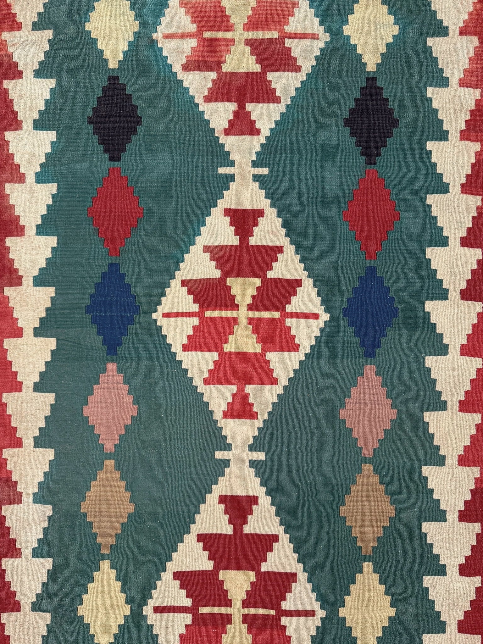 A close-up of a woven textile with a Southwestern geometric pattern featuring red, navy, pink, beige, and teal diamond and triangle motifs.