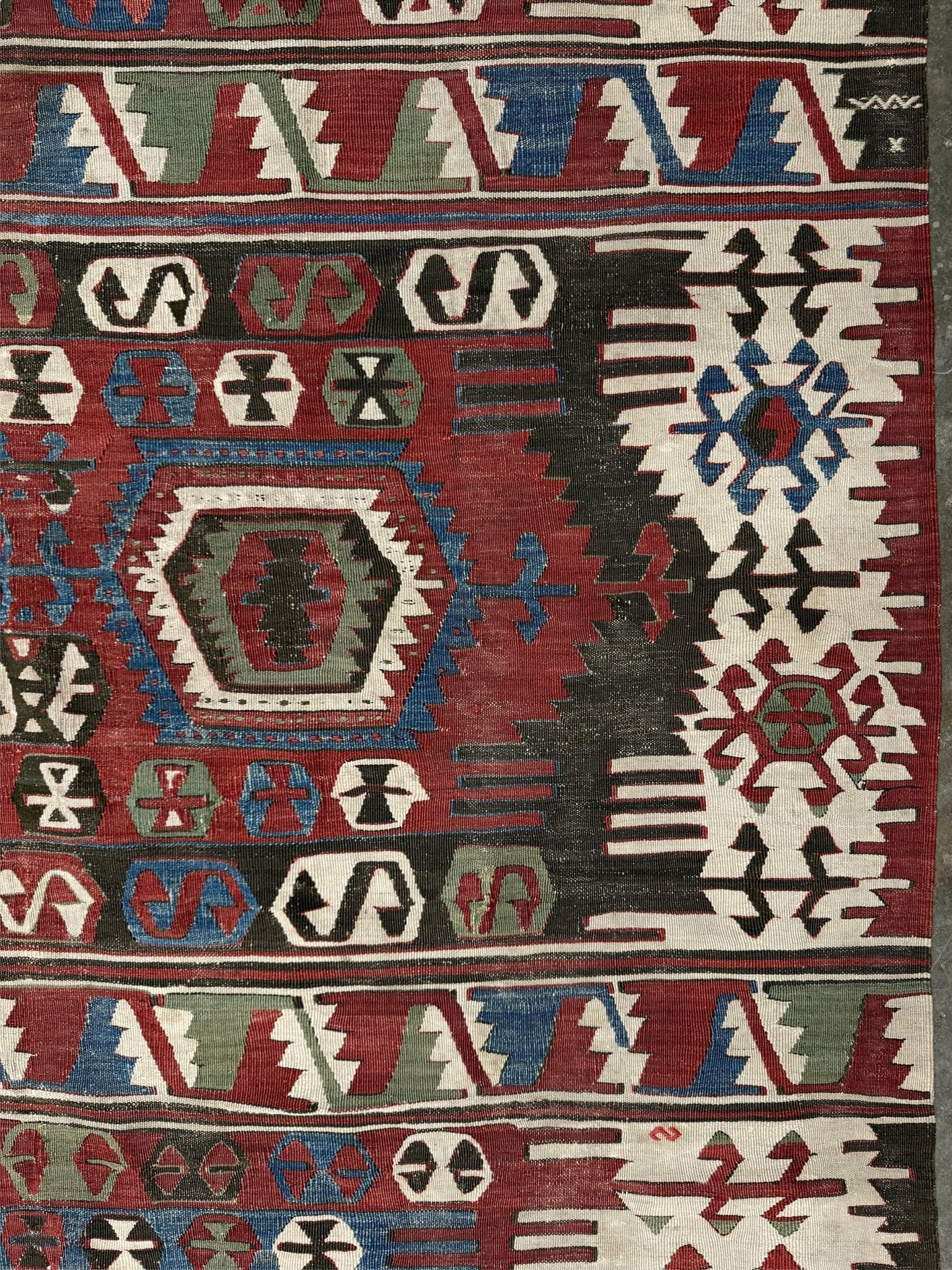 Close-up of a patterned rug with geometric designs in red, blue, and white. Antique konya turkish kilim rug 6x9 vintage tribal geometric flatweave 1930s distressed handmade anatolian wool rug san francisco bay area rug shop indigo rugs