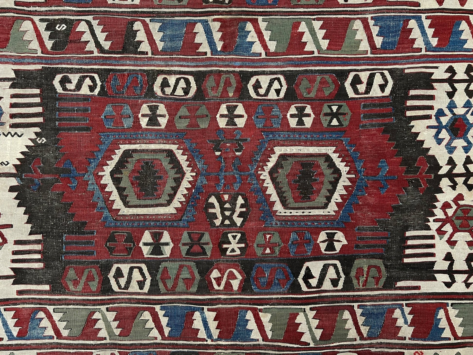 Close-up of a patterned rug with geometric designs in red, blue, and beige. Antique konya turkish kilim rug 6x9 vintage tribal geometric flatweave 1930s distressed handmade anatolian wool rug san francisco bay area rug shop indigo rugs