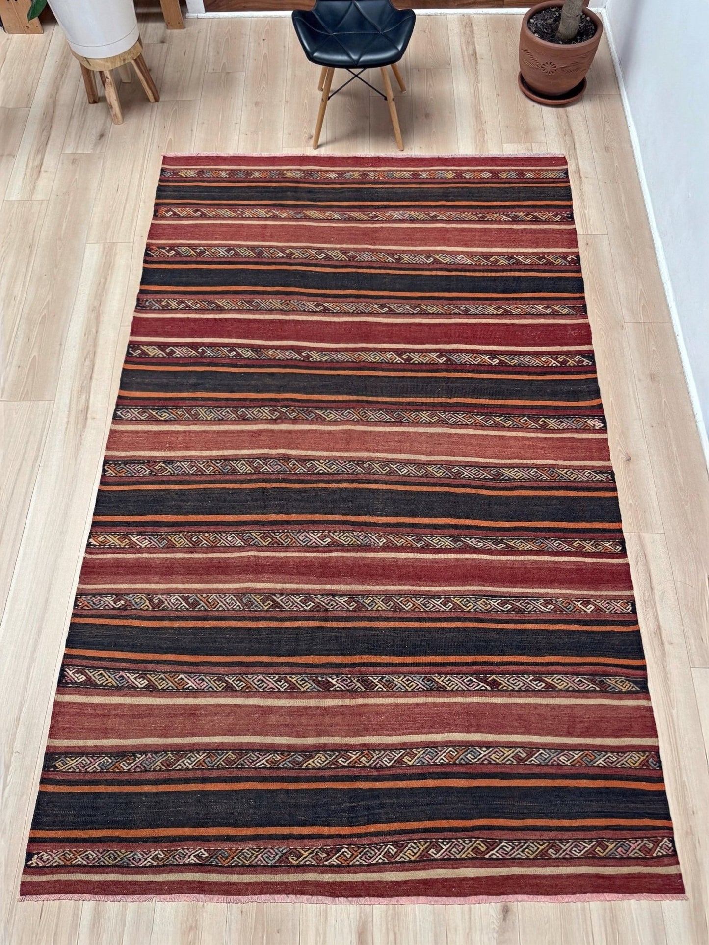 Earthy Large 6x9 vintage Turkish kilim rug with horizontal tribal stripes in madder red black and earth tones, handmade wool flatweave.