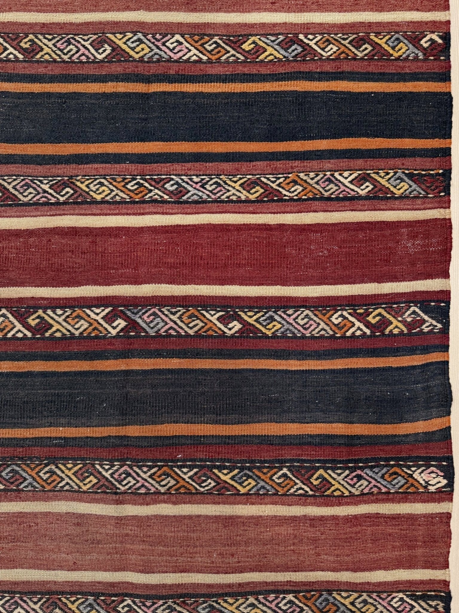Textile with geometric pattern featuring red, blue, and orange colors. Earthy Large vintage Turkish kilim rug with horizontal tribal stripes in madder red black and earth tones, handmade wool flatweave.