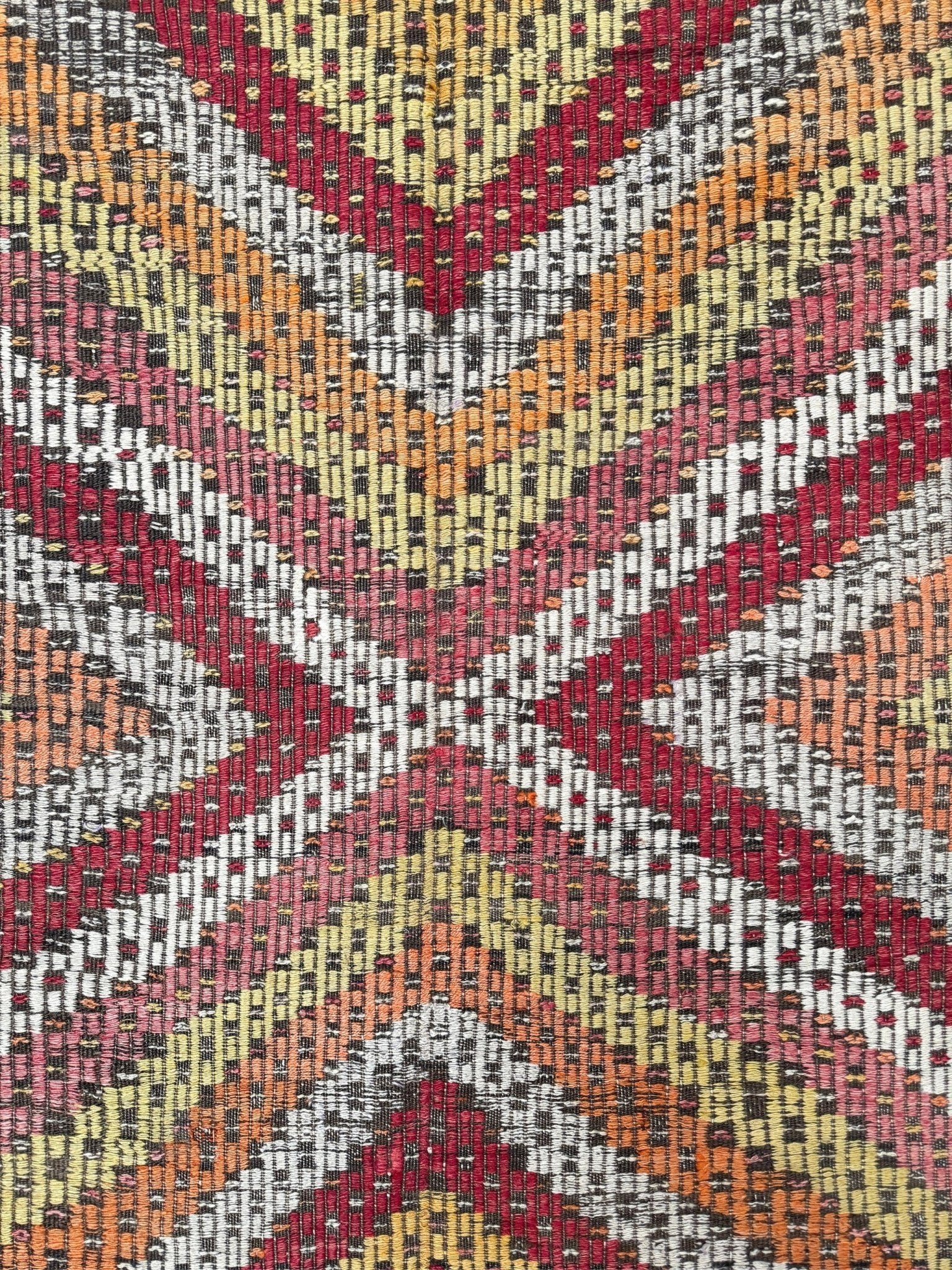 A close-up of a woven textile with a geometric chevron and cross-like pattern in red, orange, pink, beige, gray, and black.  6x9 Vintage Turkish cicim kilim rug with bold diamond pattern, handmade Turkish embroidered wool flatweave from Indigo Rugs Burlingame Bay Area.