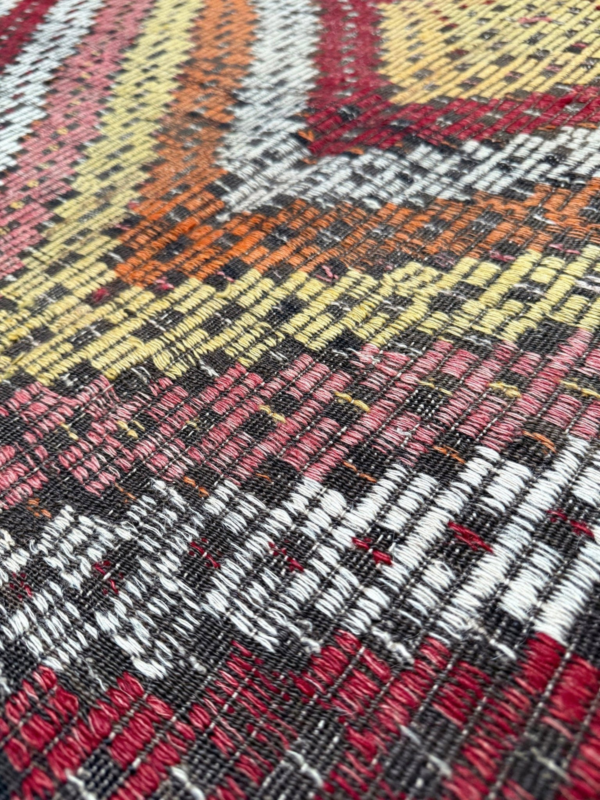 Close-up of a woven textile with a geometric pattern in black, white, red, orange, yellow, and pink.  6x9 Vintage Turkish cicim kilim rug with bold diamond pattern, handmade Turkish embroidered wool flatweave from Indigo Rugs Burlingame Bay Area.