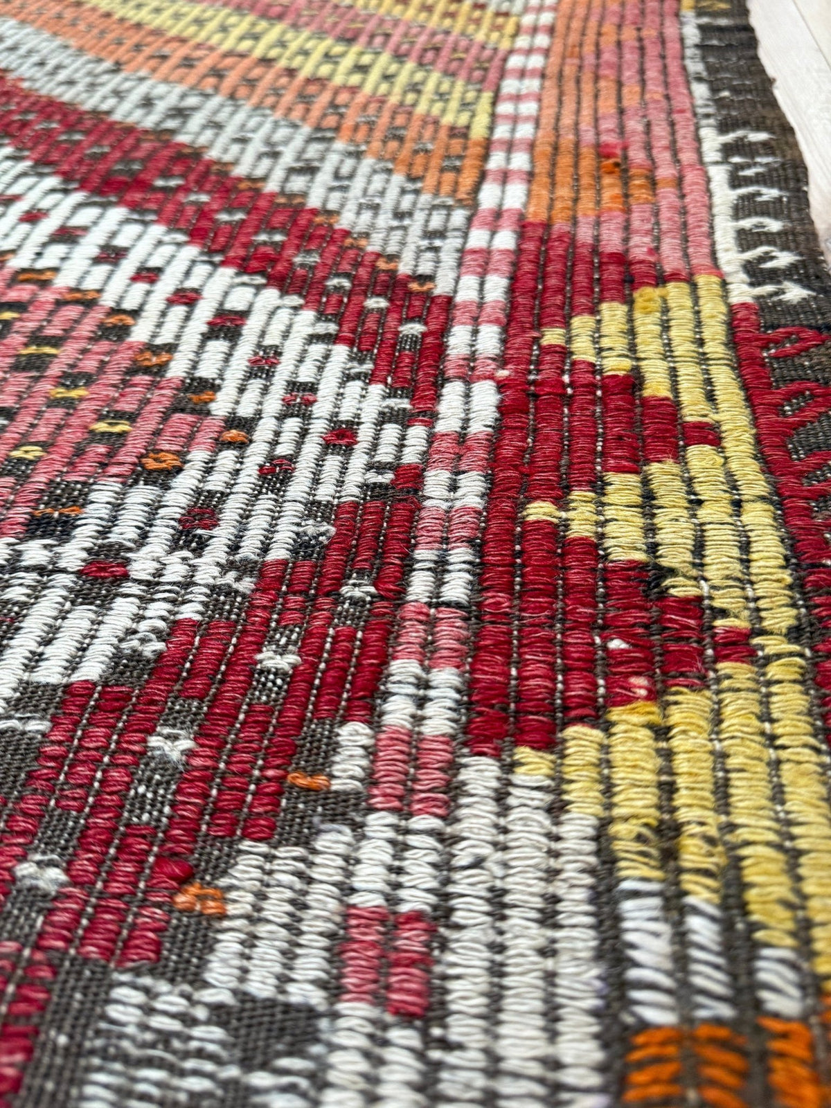 Close-up of a woven rug with a textured, chunky knit pattern featuring geometric stripes in red, yellow, white, orange, and dark gray.  6x9 Vintage Turkish cicim kilim rug with bold diamond pattern, handmade Turkish embroidered wool flatweave from Indigo Rugs Burlingame Bay Area.