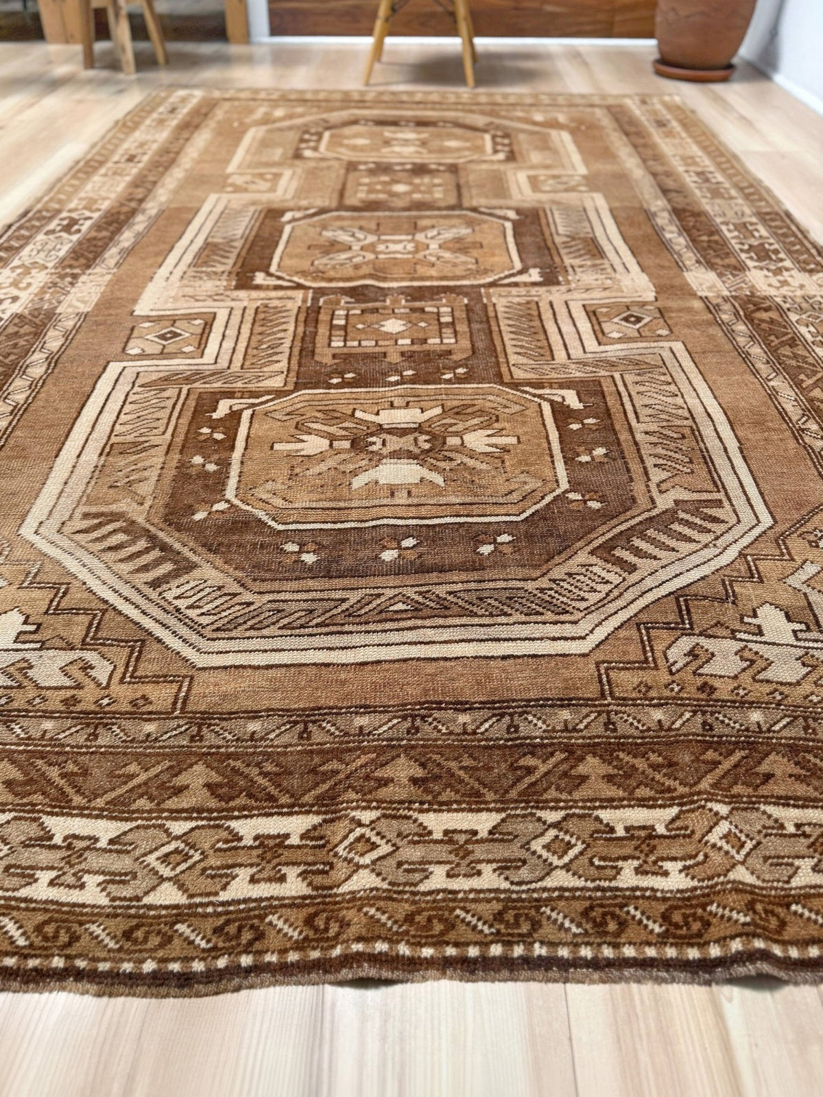 A traditional oriental-style area rug with an intricate geometric and medallion pattern in shades of brown, beige, and cream, laid out on a light-colored wooden floor.