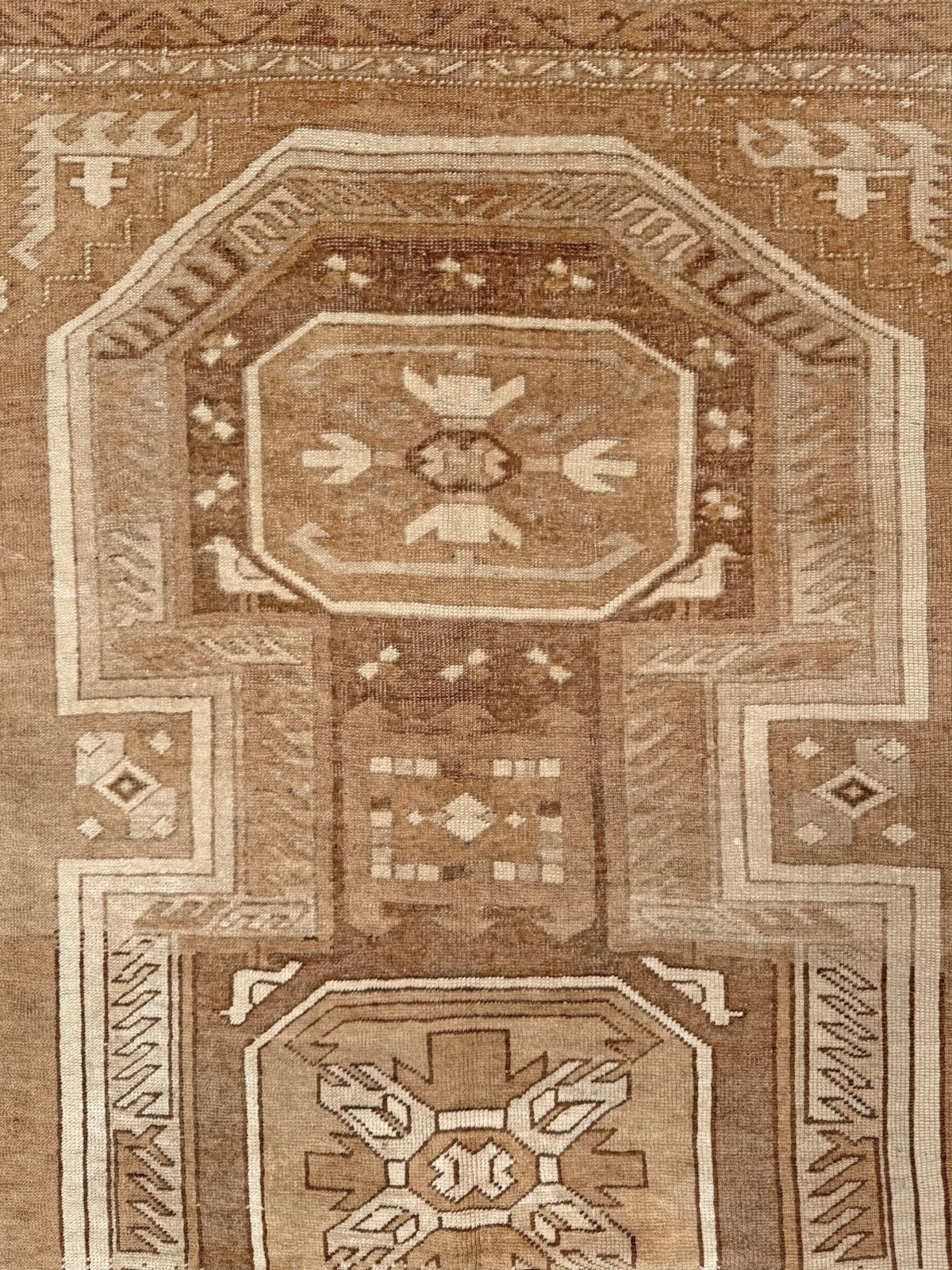 A close-up of a traditional patterned rug in earthy brown and beige tones, showing geometric and floral motifs.