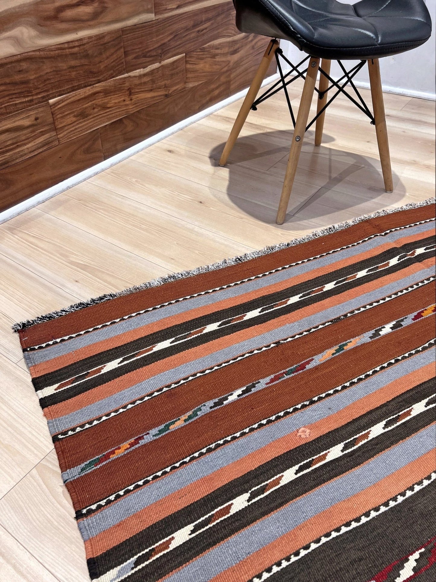 Striped area rug on a wooden floor with a chair in the background. Vintage Caucasian kilim rug with horizontal tribal stripes in rust, brown, gray, and ivory tones, handwoven wool flatweave rug 6x9
