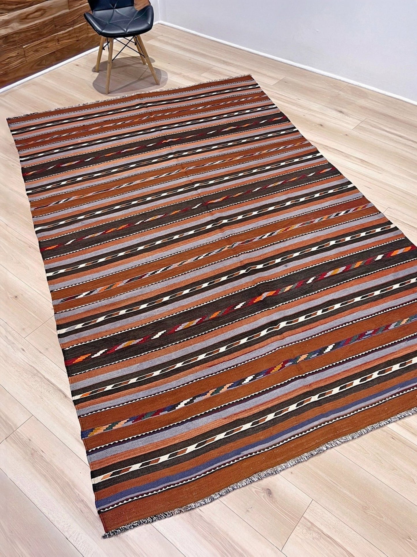 Striped area rug on a wooden floor with a chair partially visible. Vintage Caucasian kilim rug with horizontal tribal stripes in rust, brown, gray, and ivory tones, handwoven wool flatweave rug 6x9