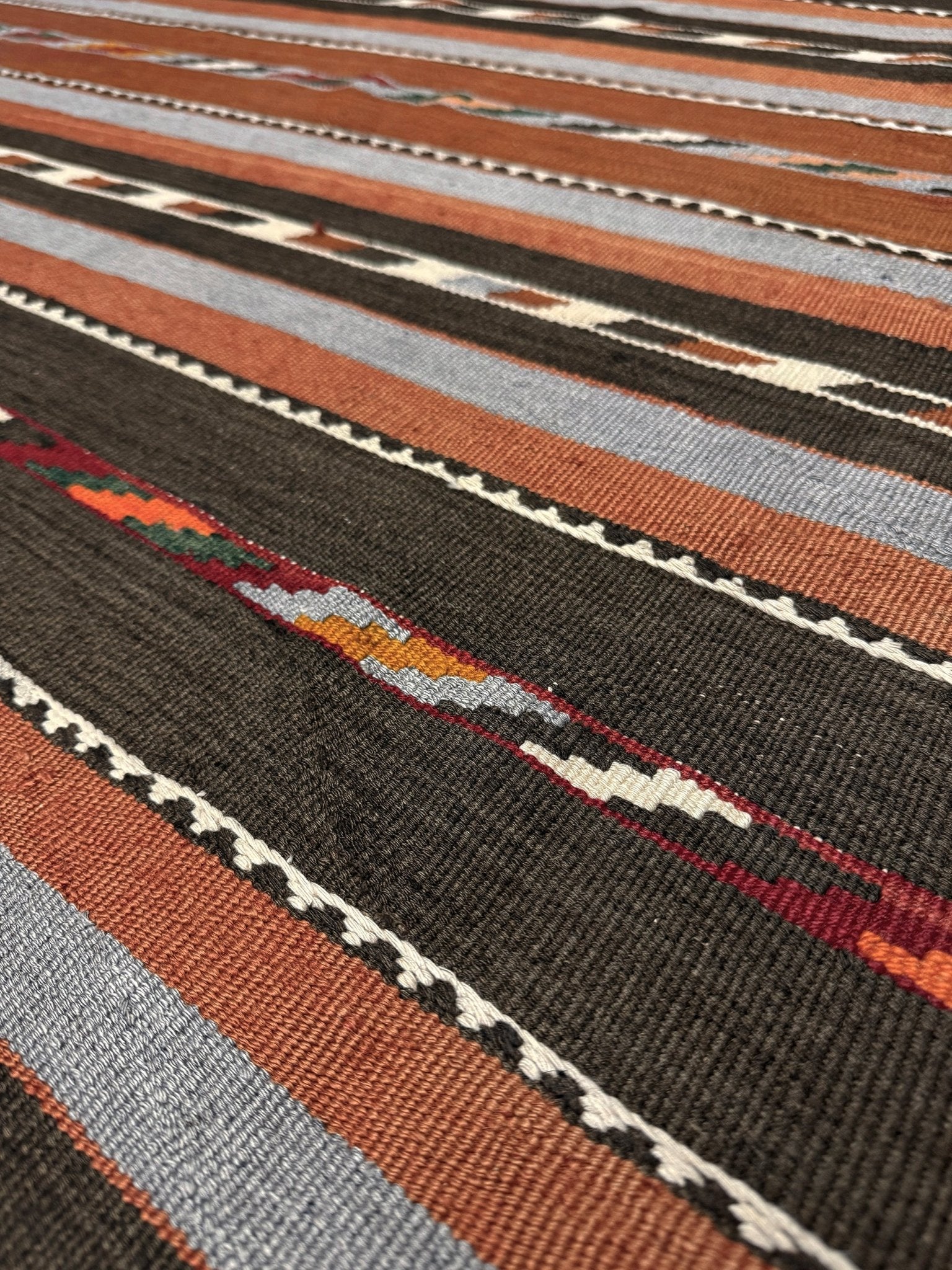Close-up of a patterned rug with brown, gray, and beige stripes. Vintage Caucasian kilim rug with horizontal tribal stripes in rust, brown, gray, and ivory tones, handwoven wool flatweave rug 6x9