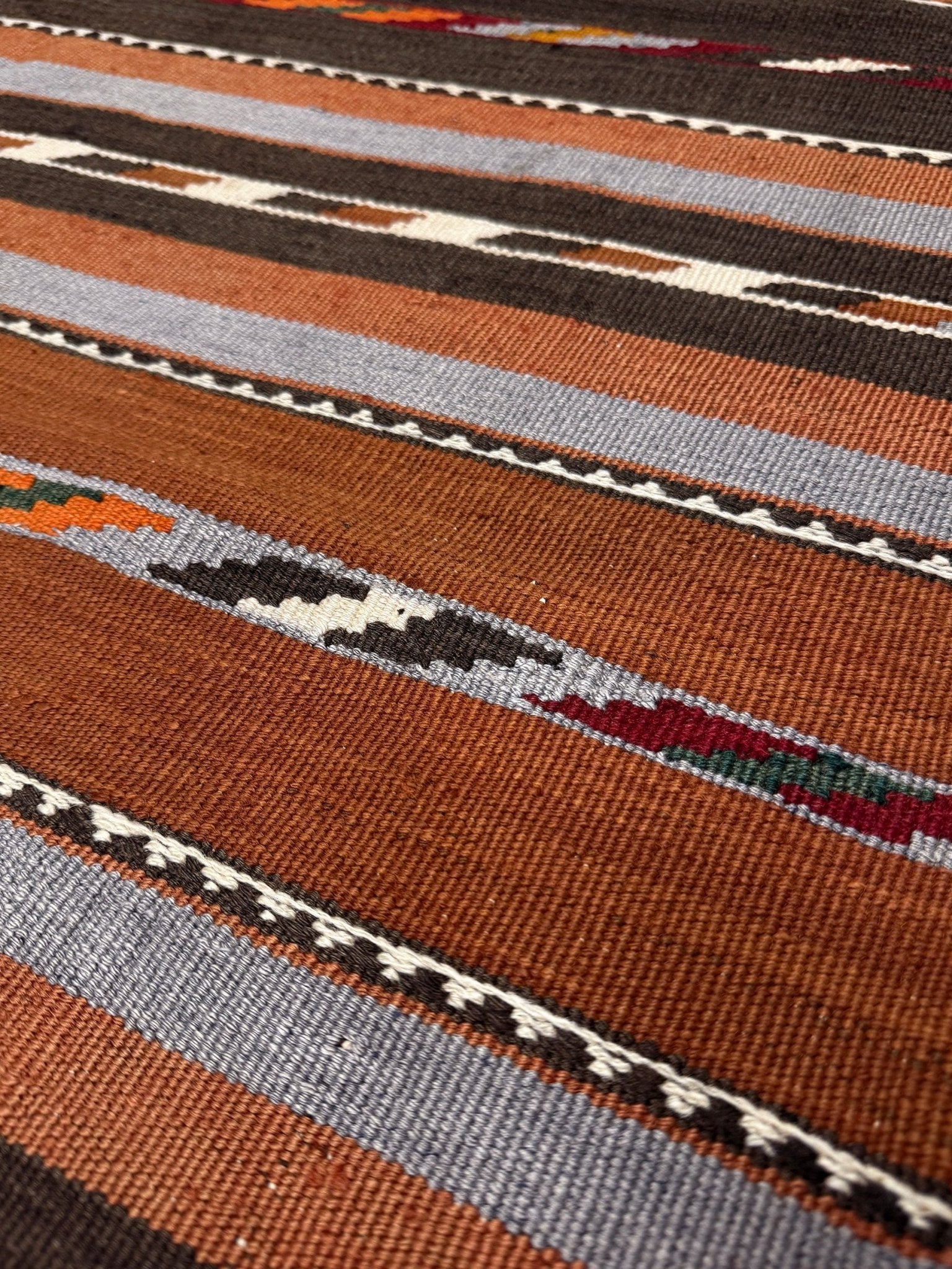 Close-up of a patterned fabric with brown, gray, and multicolor stripes. Vintage Caucasian kilim rug with horizontal tribal stripes in rust, brown, gray, and ivory tones, handwoven wool flatweave rug 6x9
