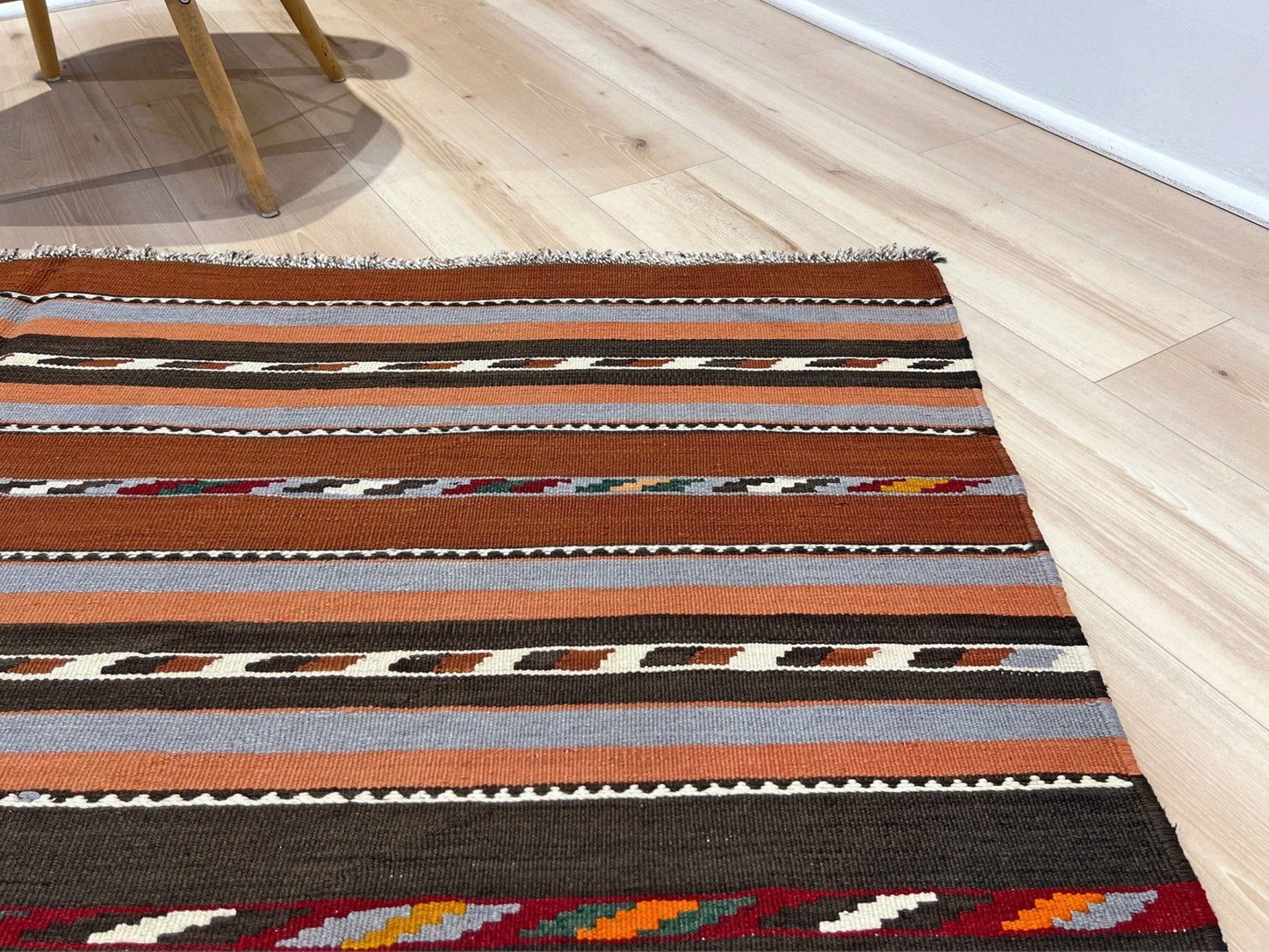Striped patterned rug on a wooden floor. Vintage Caucasian kilim rug with horizontal tribal stripes in rust, brown, gray, and ivory tones, handwoven wool flatweave rug 6x9