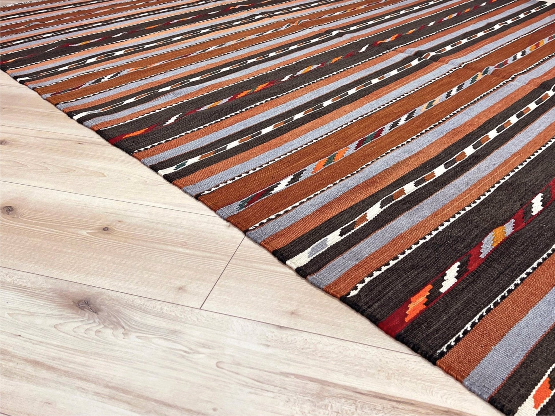 Striped area rug with brown, black, and gray pattern on a wooden floor. Vintage Caucasian kilim rug with horizontal tribal stripes in rust, brown, gray, and ivory tones, handwoven wool flatweave rug 6x9