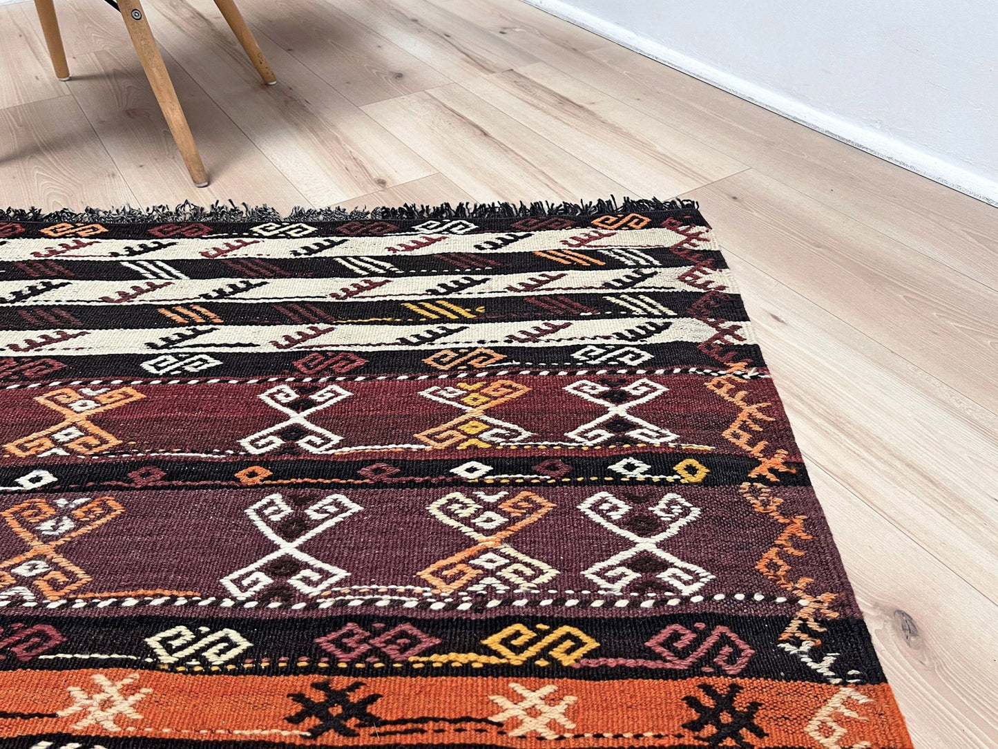 Patterned rug on a wooden floor. Vintage Kars kilim rug from Eastern Turkey, 6x8, with horizontal tribal bands in brown, ivory, rust, and charcoal geometric motifs.