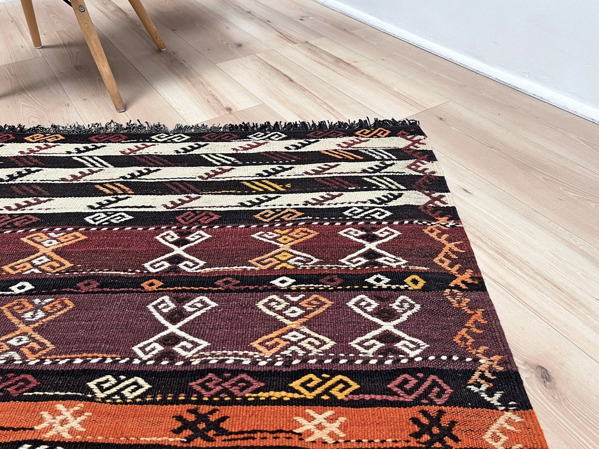 Patterned rug on a wooden floor. Vintage Kars kilim rug from Eastern Turkey, 6x8, with horizontal tribal bands in brown, ivory, rust, and charcoal geometric motifs.