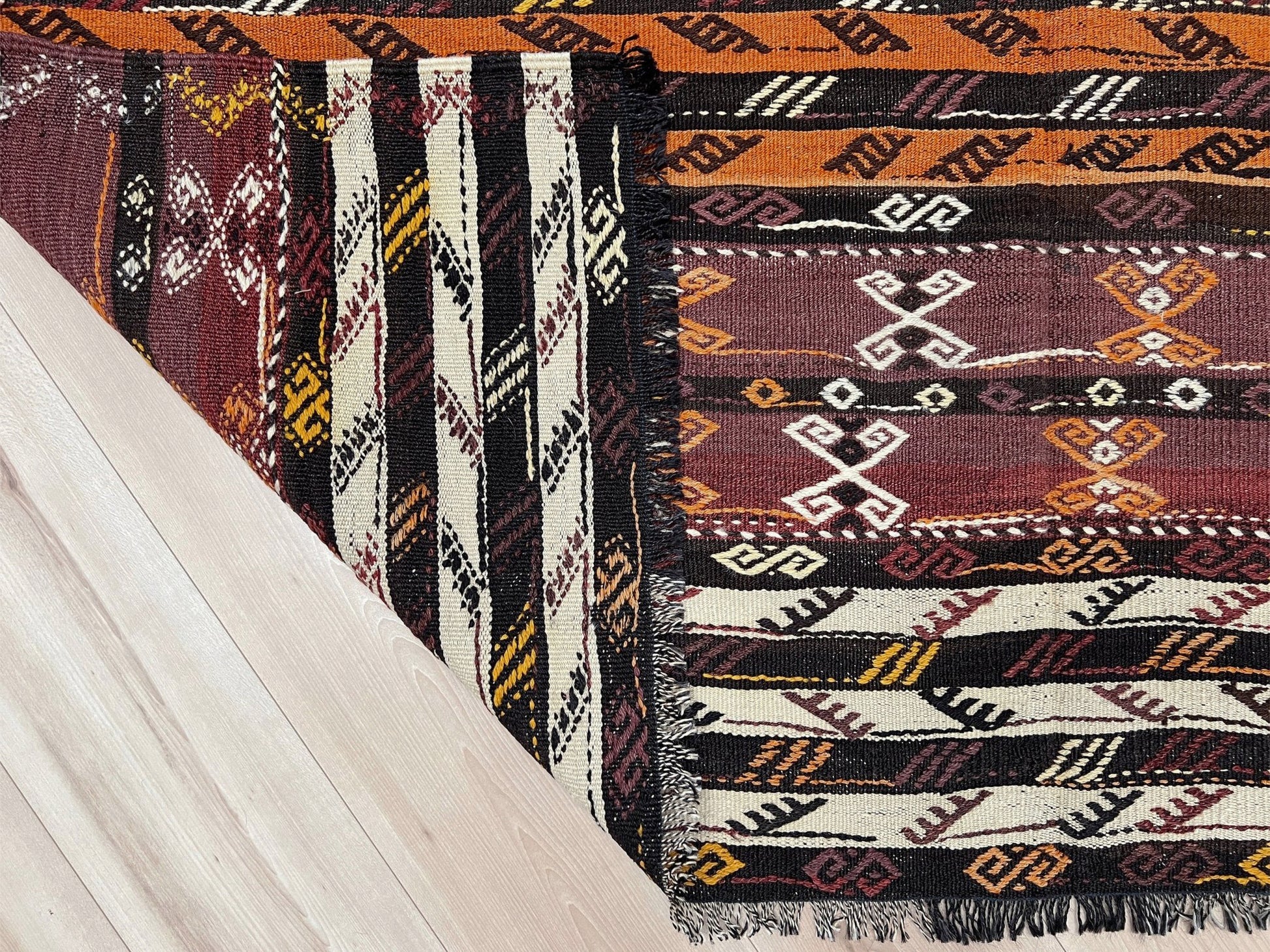 Patterned rug with geometric design on a wooden floor. Vintage Kars kilim rug from Eastern Turkey, 6x8, with horizontal tribal bands in brown, ivory, rust, and charcoal geometric motifs.